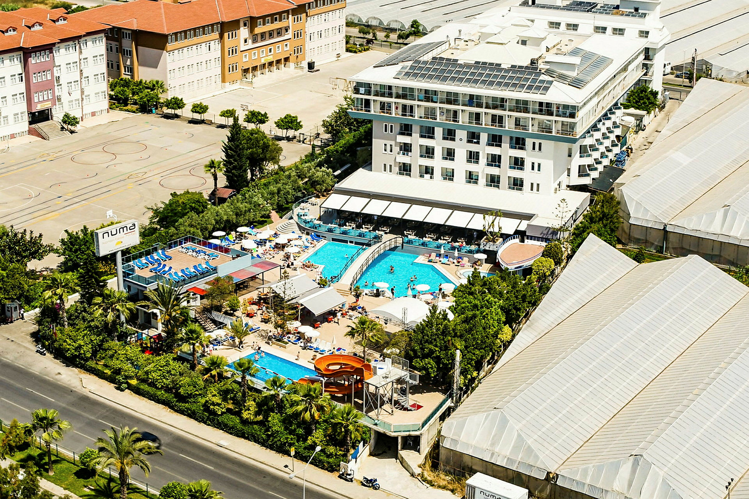Flygfoto av ett hotell med utomhuspooler och omgivande byggnader. (AI-genererad text)