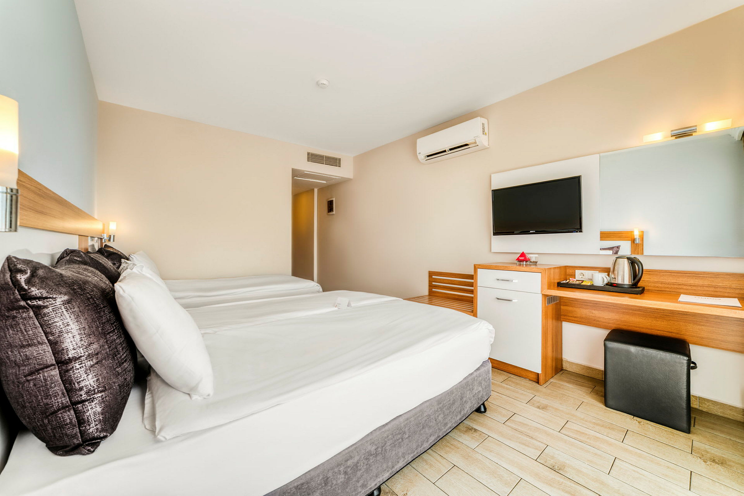 Ett hotellrum med två sängar, ett skrivbord, en spegel och en väggmonterad TV. (AI-genererad text)