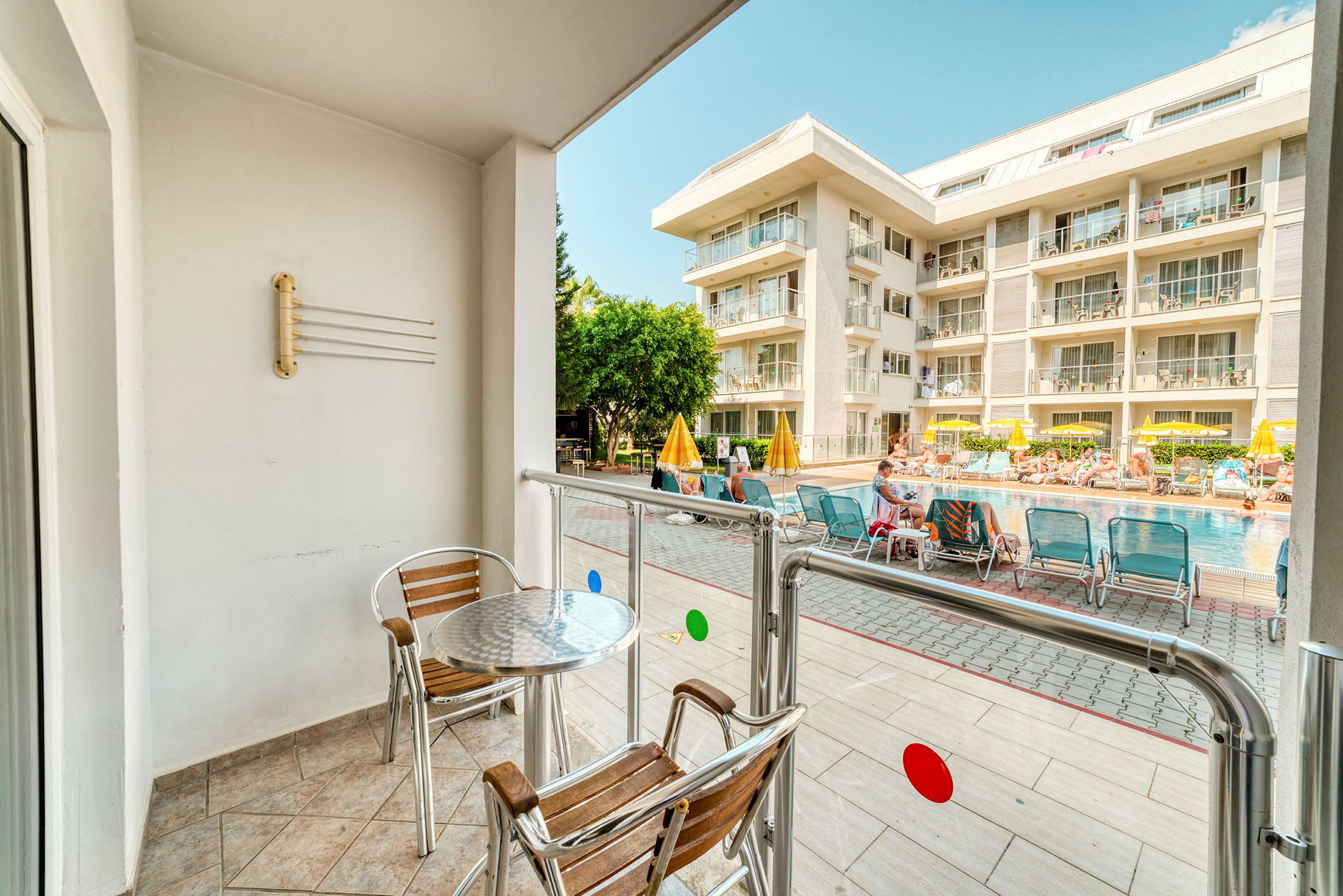 En balkong med bord och stolar vetter mot en pool och ett hotell. (AI-genererad text)