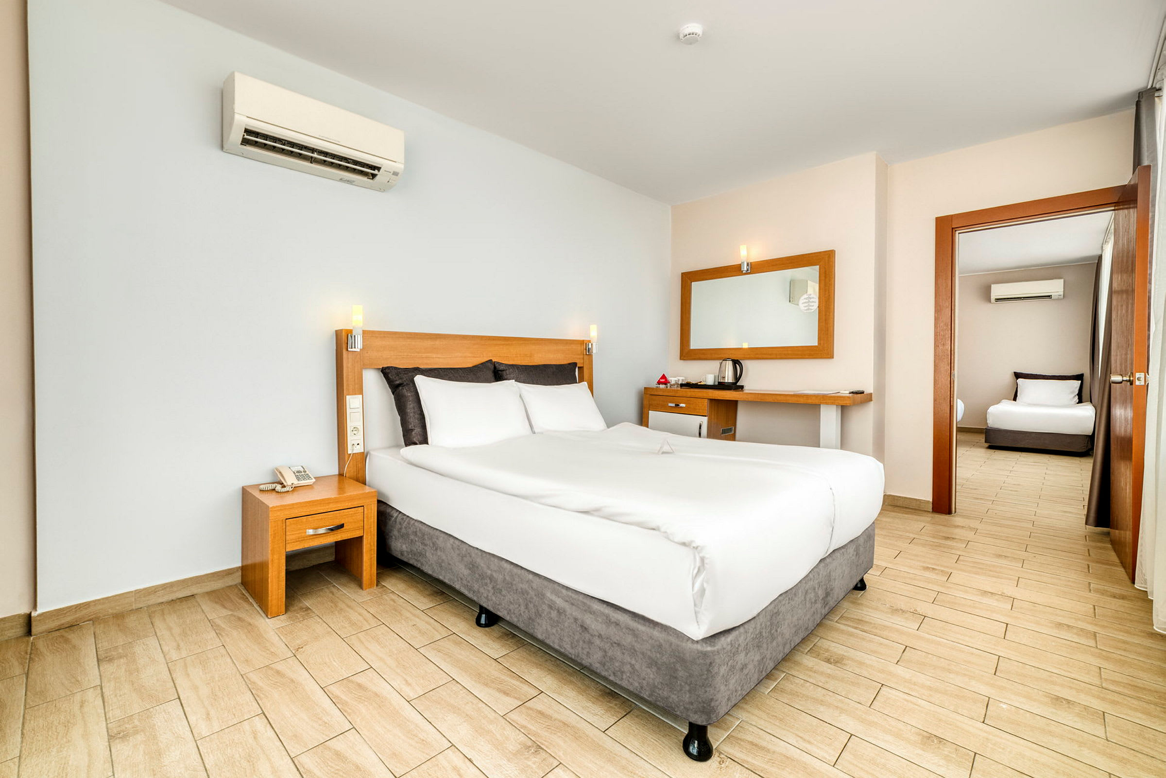 Hotellrum med en dubbelsäng, sängbord och skrivbord samt en dörr som leder till ett annat rum. (AI-genererad text)