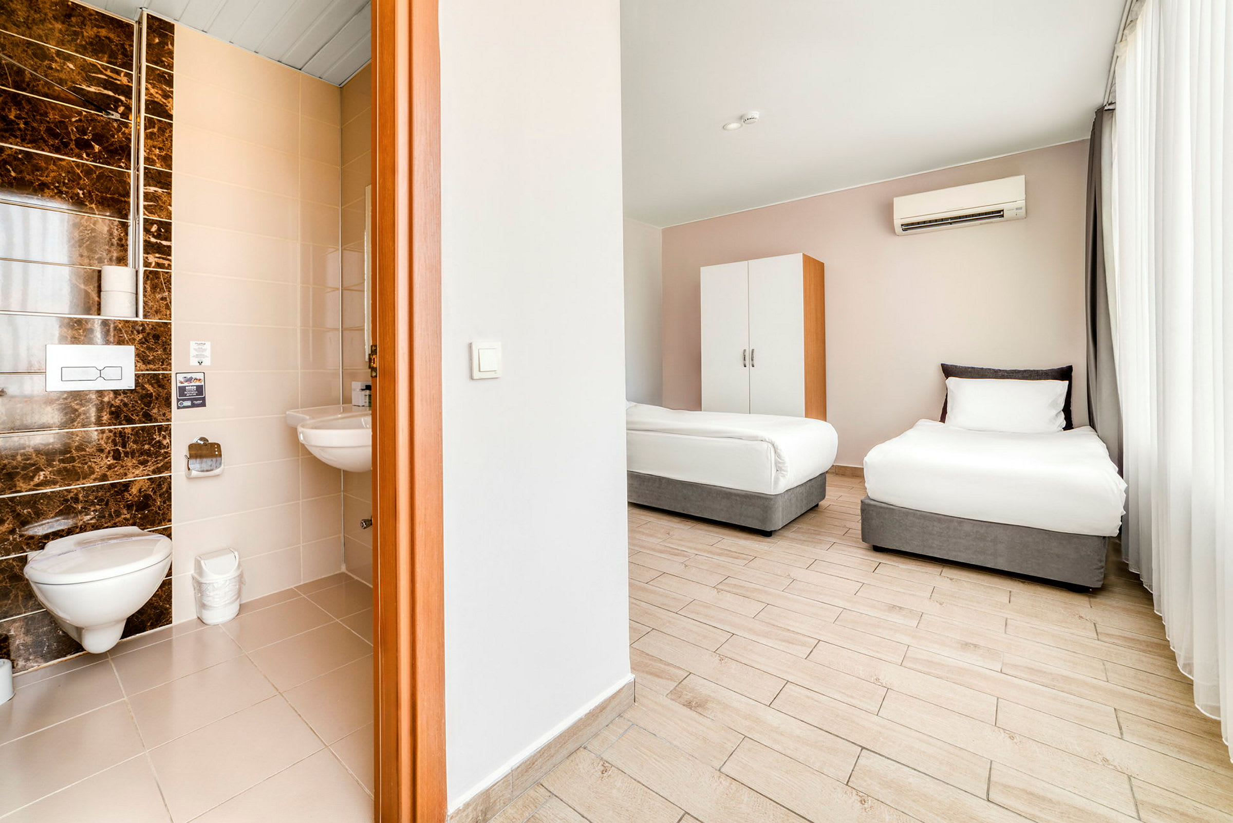 Ett hotellrum med två enkelsängar och en utsikt mot ett delvis synligt kök och badrum. (AI-genererad text)