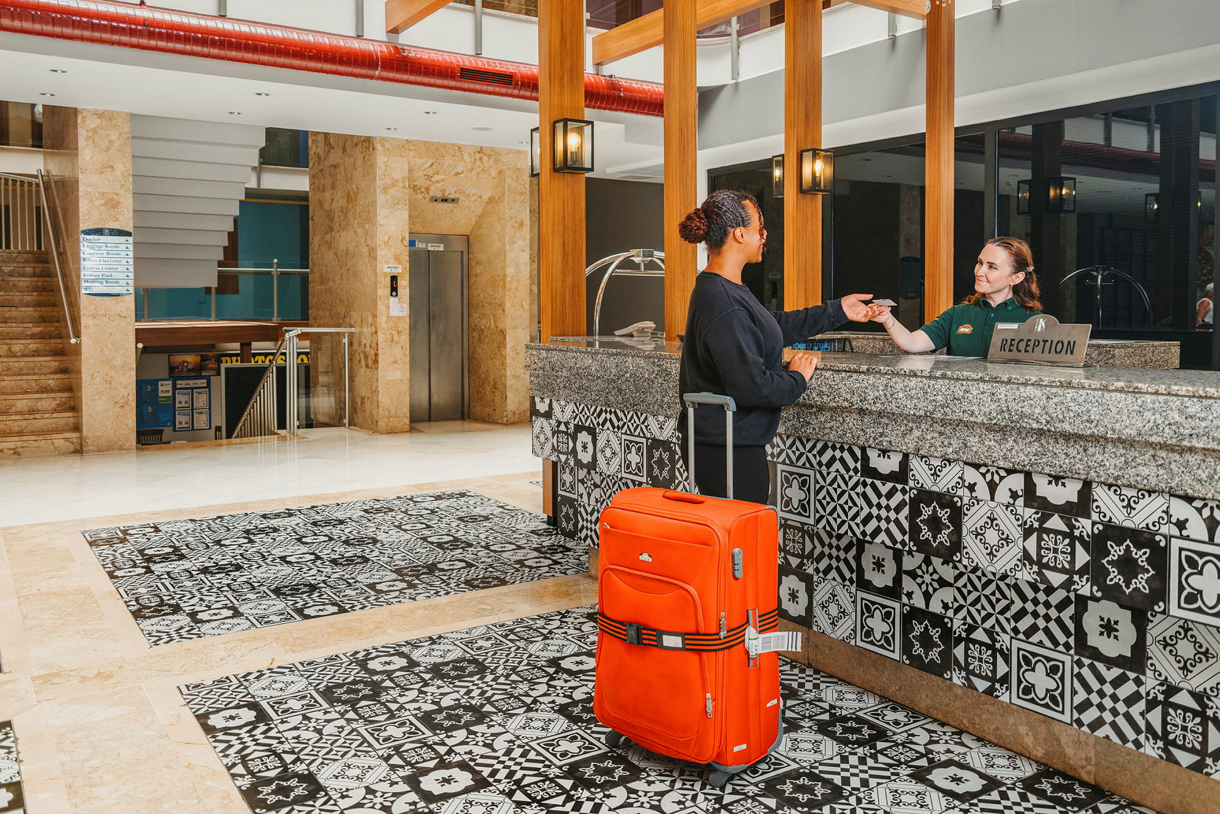 En person vid en hotellreception med en orange resväska. (AI-genererad text)