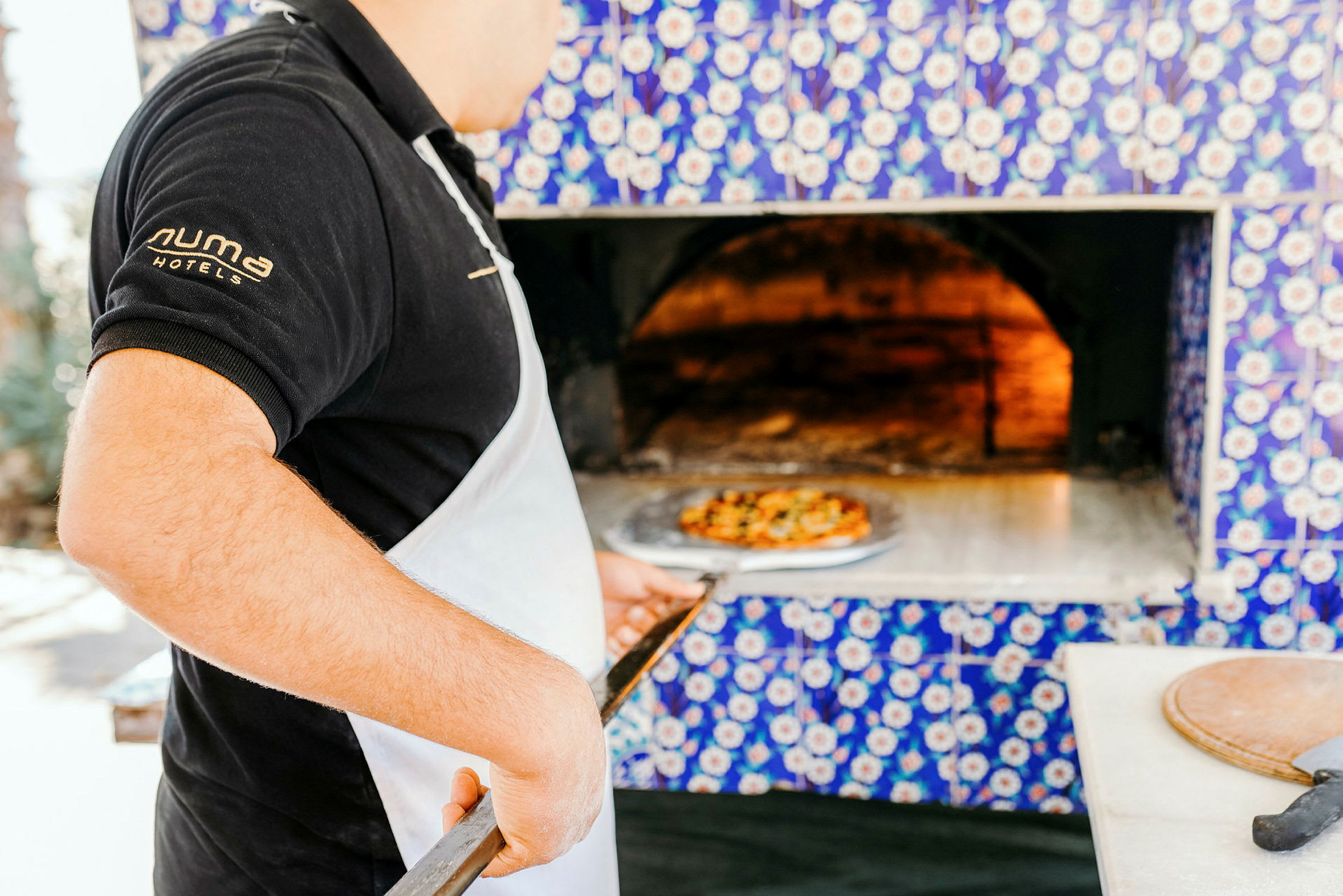 Person håller pizzaspade framför vedugn. (AI-genererad text)