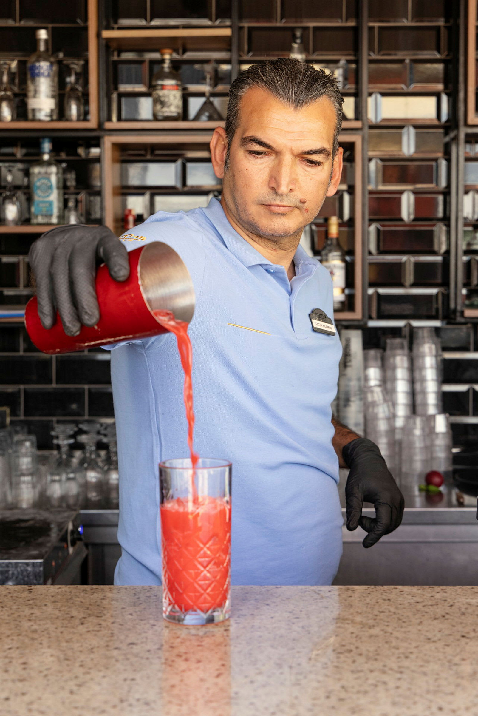En bartender häller en röd dryck från en shaker i ett glas. (AI-genererad text)