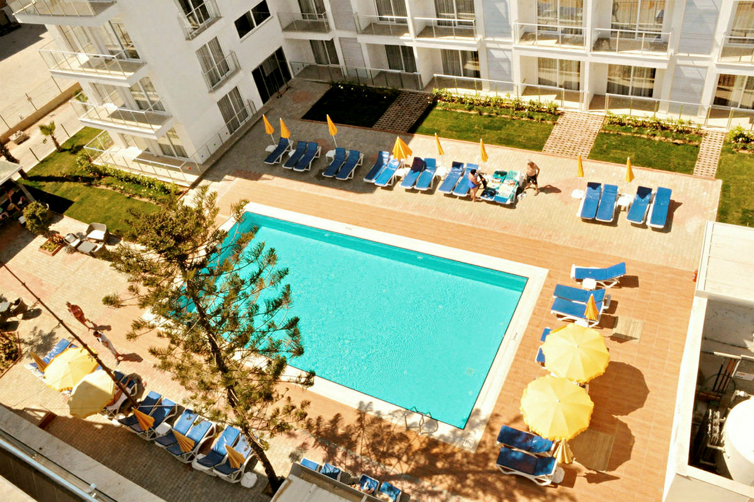 Vy över en hotellpool omgiven av solstolar och gult parasoll. (AI-genererad text)