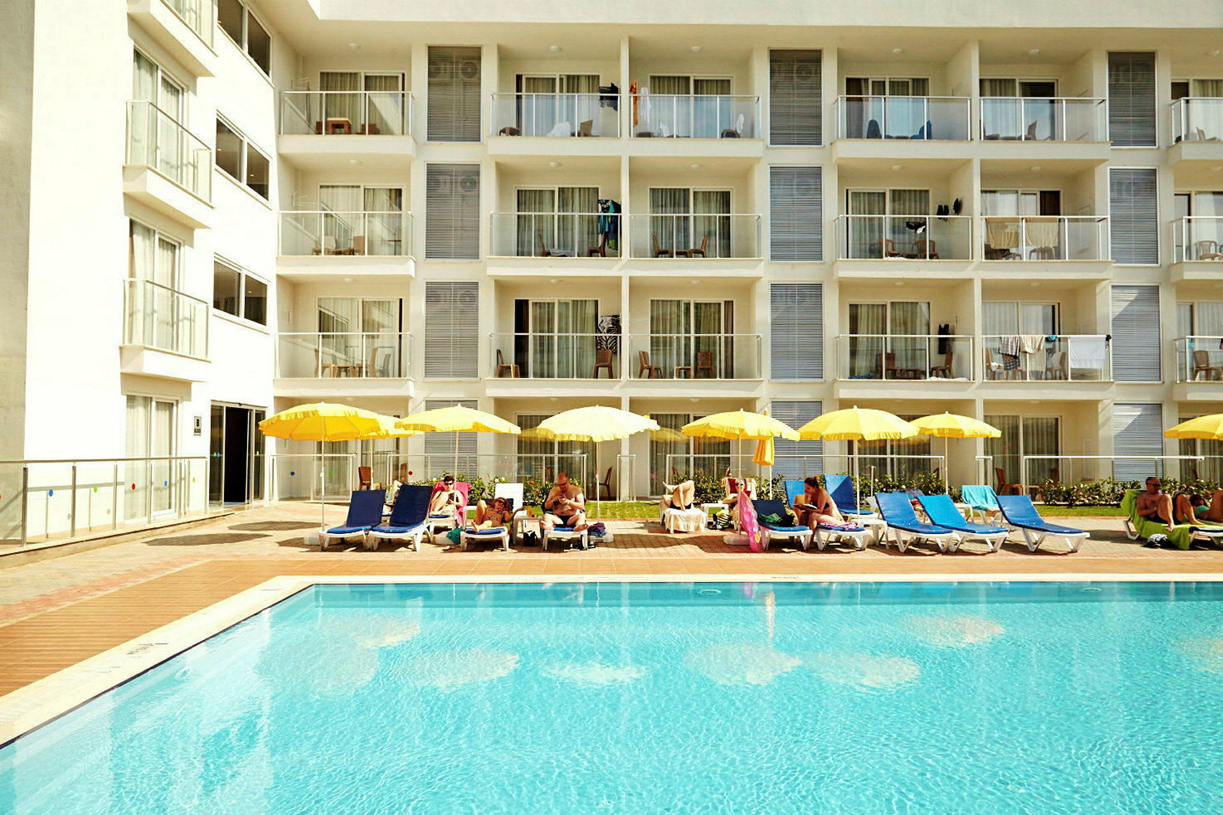 Utomhuspool med solstolar och parasoller framför ett hotell. (AI-genererad text)