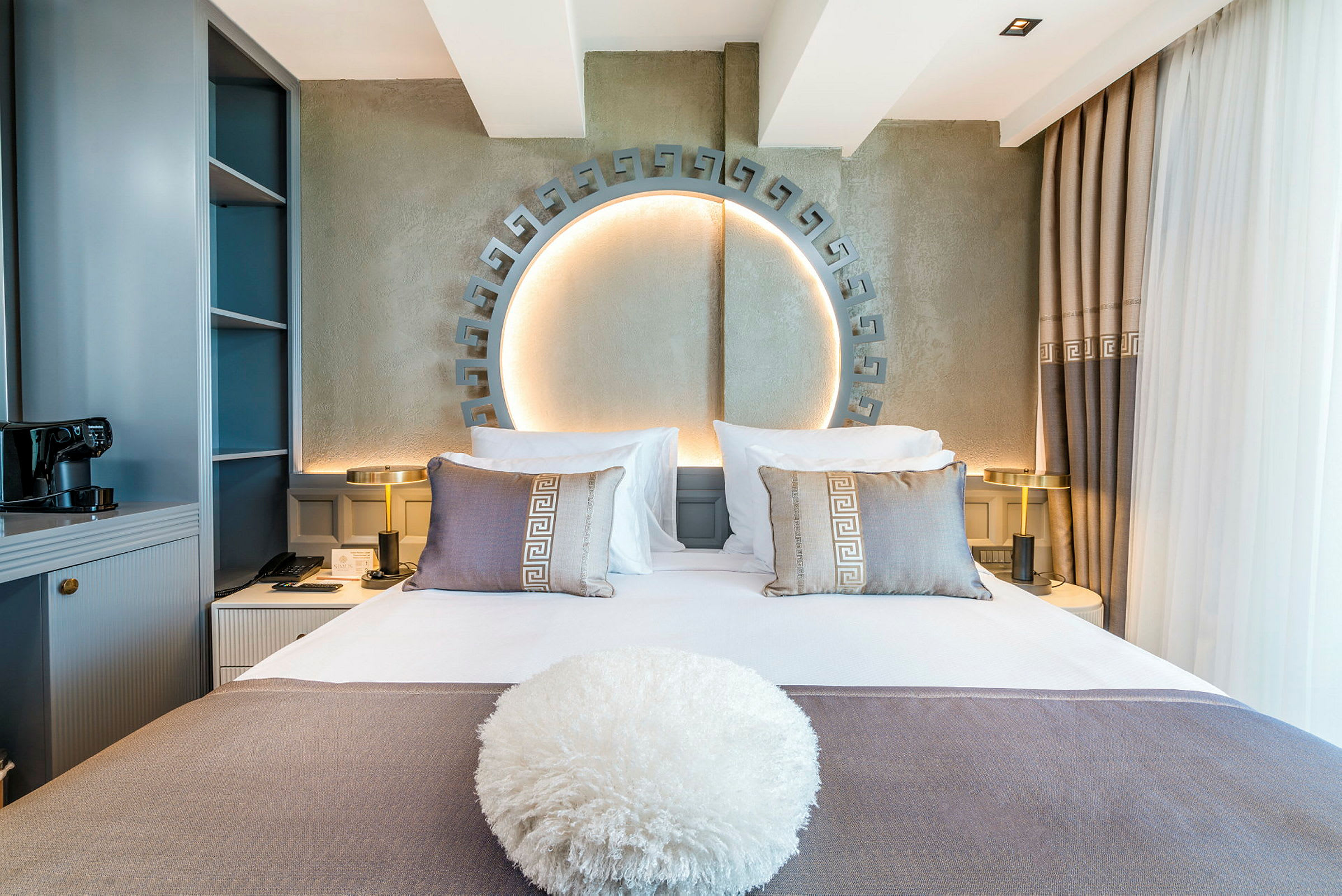 Bild på ett hotellrum med en dubbelsäng dekorerad med kuddar och en prydnadskudde framför. Bakom sängen finns en belyst dekorativ design. (AI-genererad text)