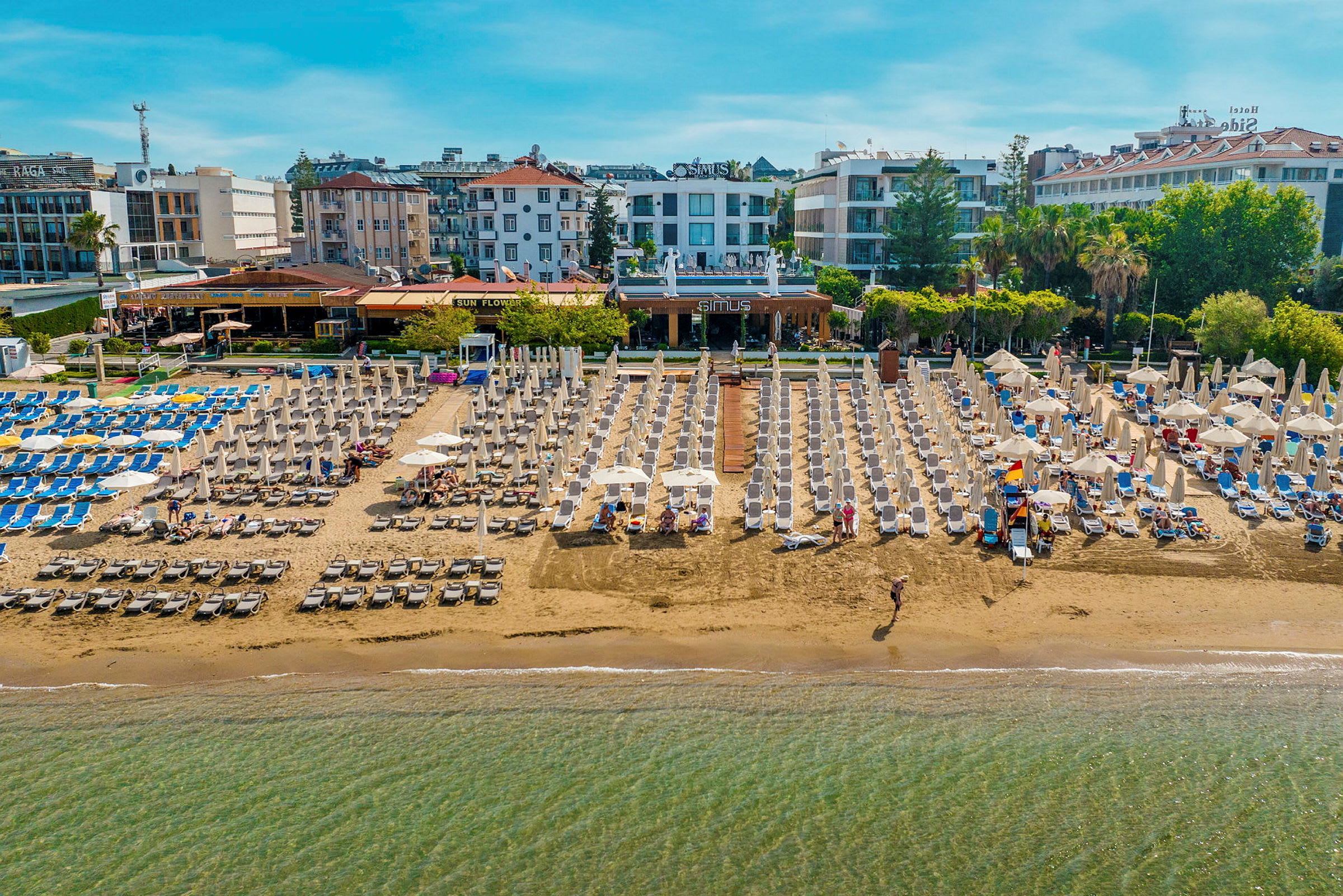 Strand med solsängar och parasoller, omgiven av hotell och byggnader. (AI-genererad text)