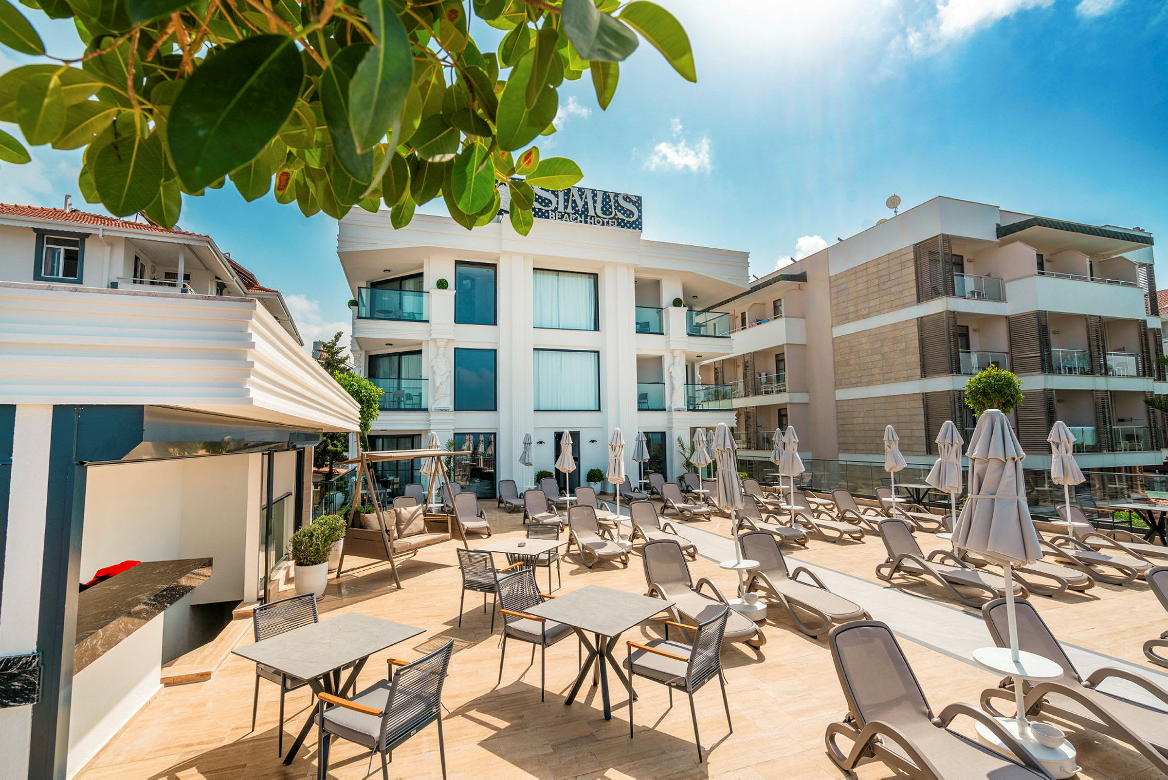 Bild på hotellområde med solstolar och parasoll utomhus samt byggnader i bakgrunden. (AI-genererad text)