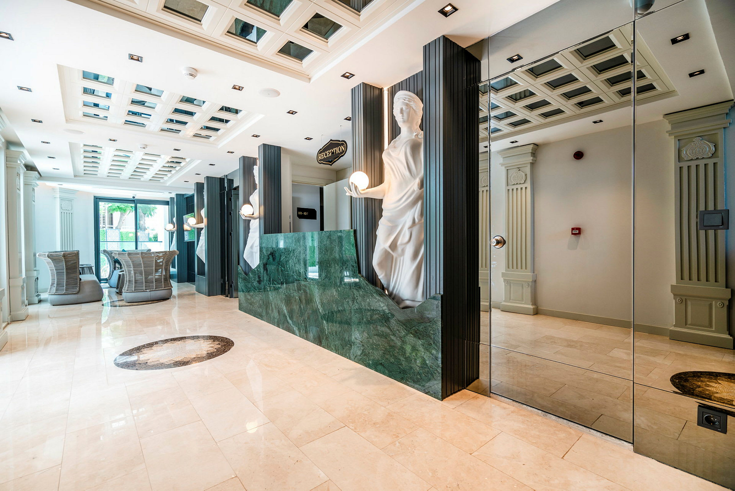 Ett hotellreceptionsområde med marmorgolv, en grön receptiondisk och en dekorativ staty bredvid. (AI-genererad text)