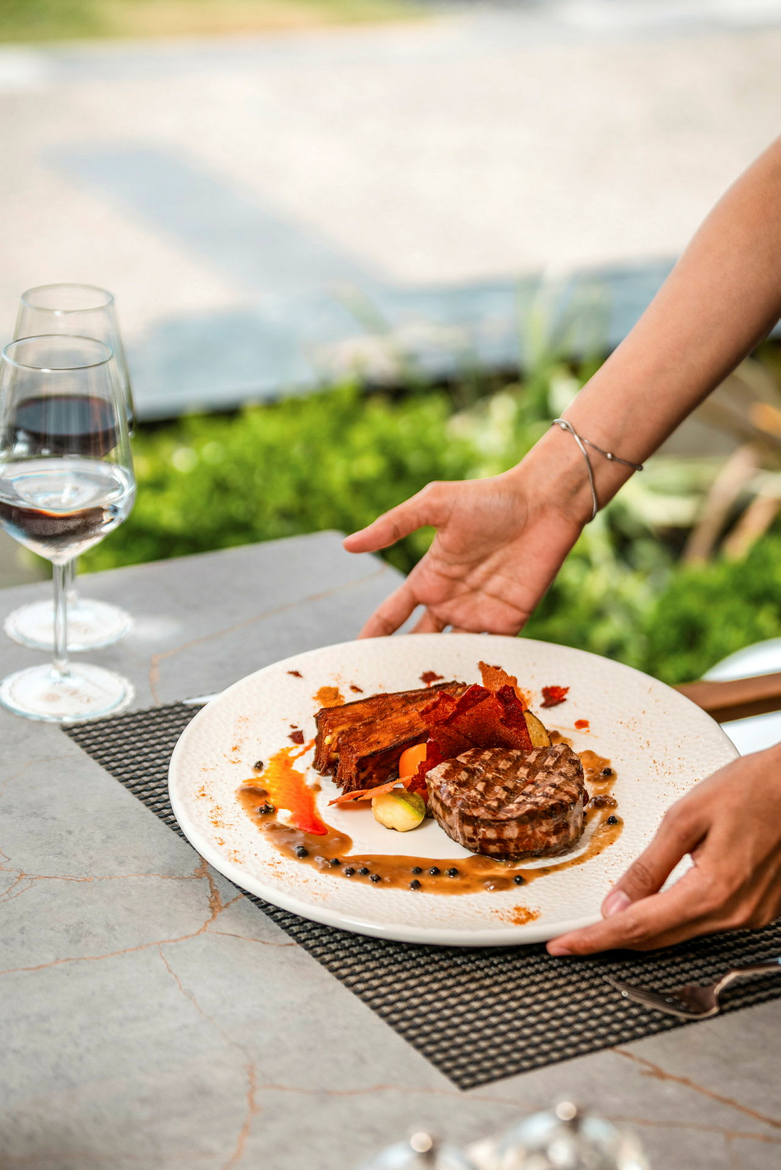 En person serverar en tallrik med kött och tillbehör vid ett bord. (AI-genererad text)