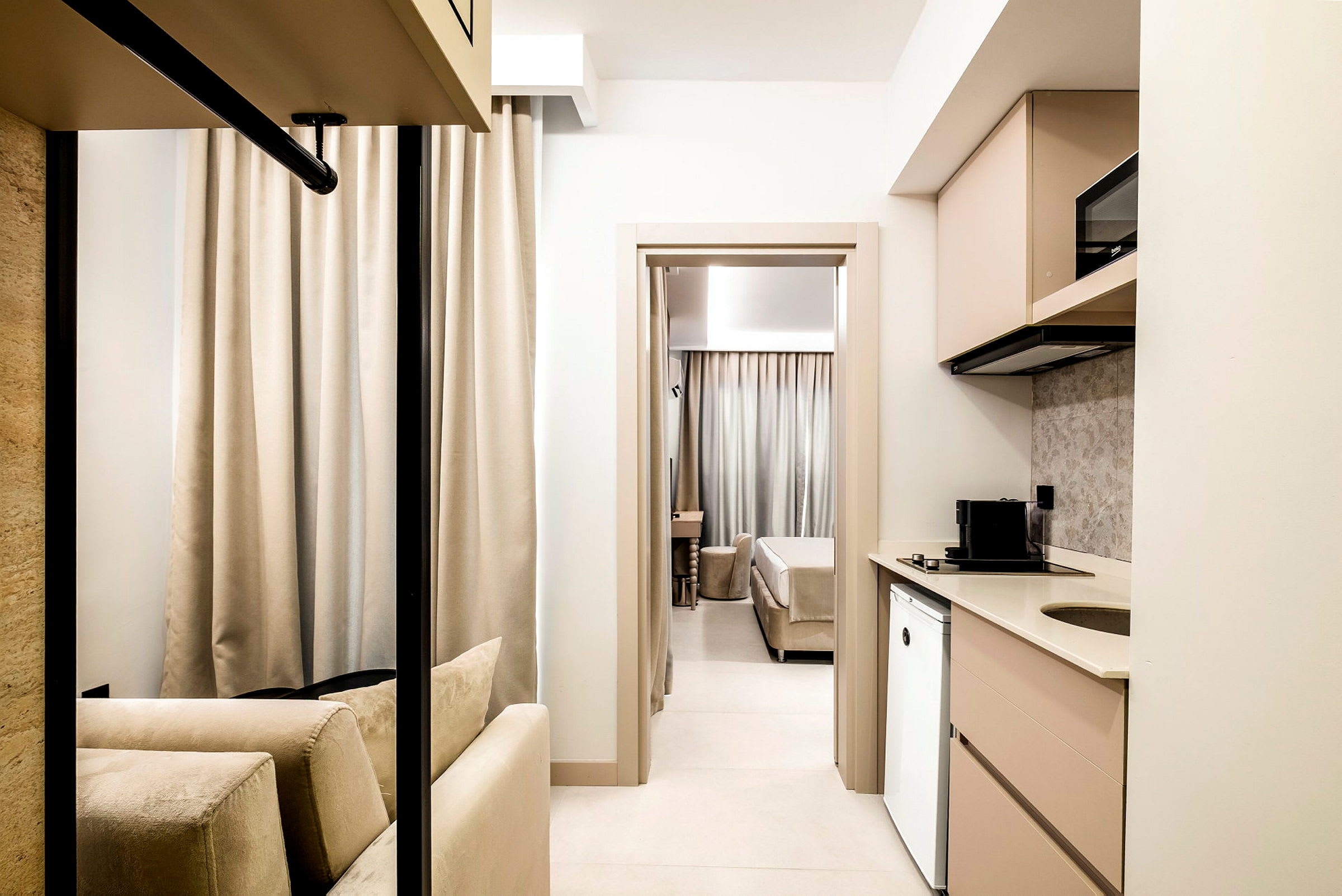 Ett ljust och modernt hotellrum med ett köksområde till höger och en bekväm sittgrupp i förgrunden, samt en sovplats i bakgrunden. (AI-genererad text)