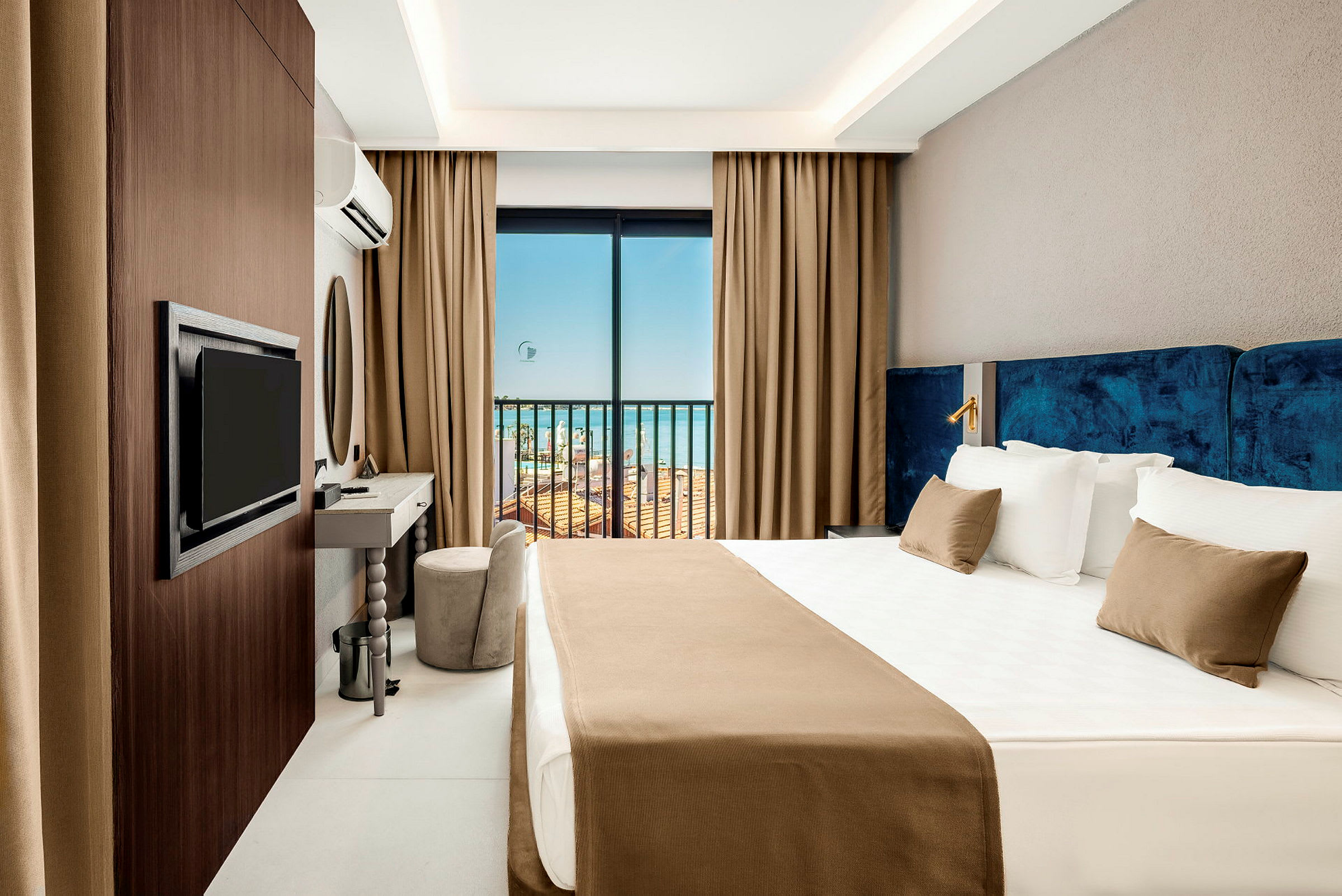 Ett hotellrum med en stor säng, TV, skrivbord och en balkongdörr som vetter mot havet. (AI-genererad text)