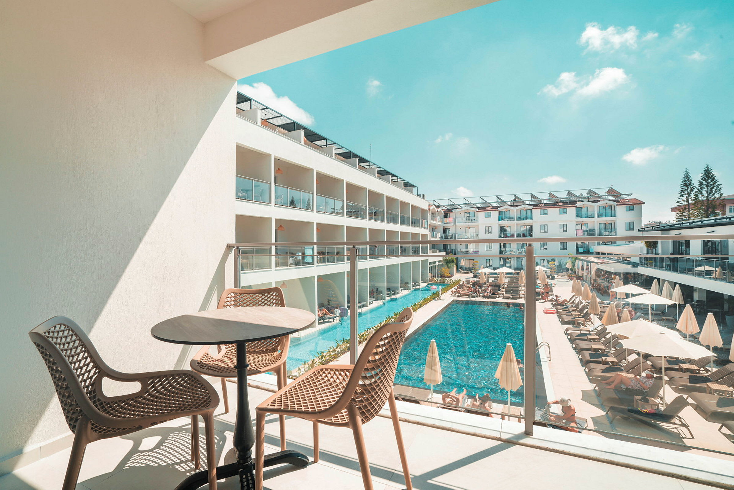 Utsikt från en balkong mot en pool och hotellbyggnader. (AI-genererad text)