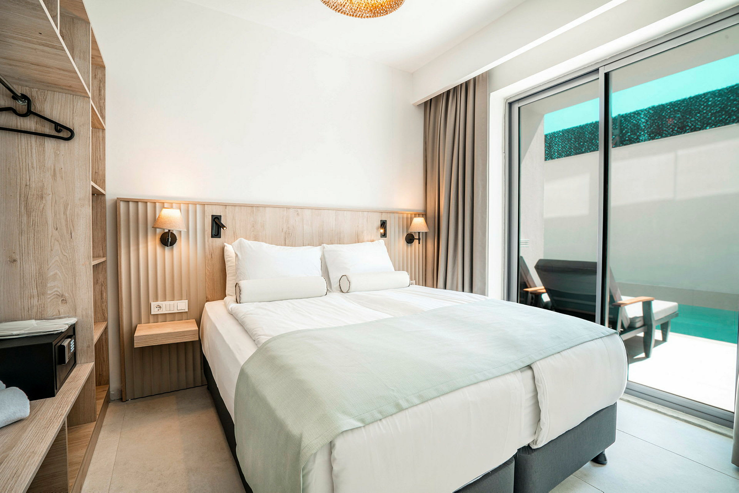 Ett hotellrum med en dubbelsäng, lådor och en balkong med utsikt mot en pool. (AI-genererad text)