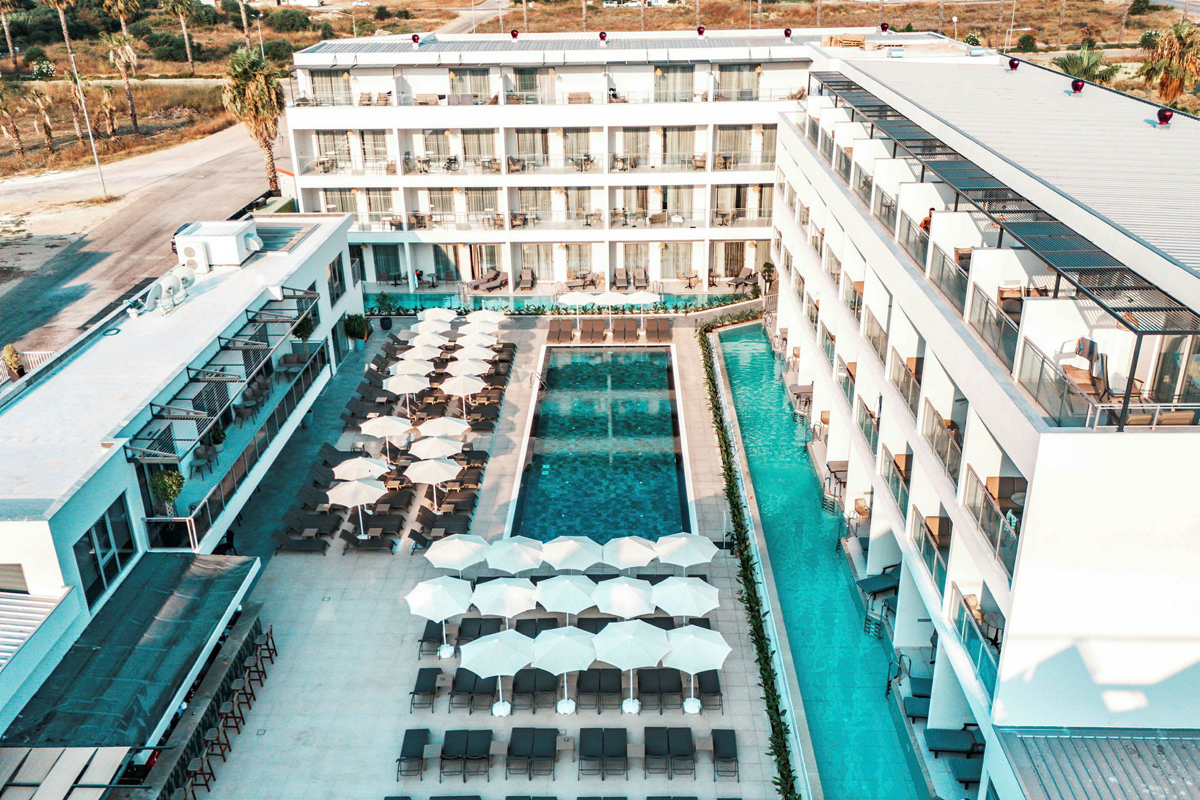 Hotellområde med byggnader runt en pool, solstolar och parasoller. (AI-genererad text)