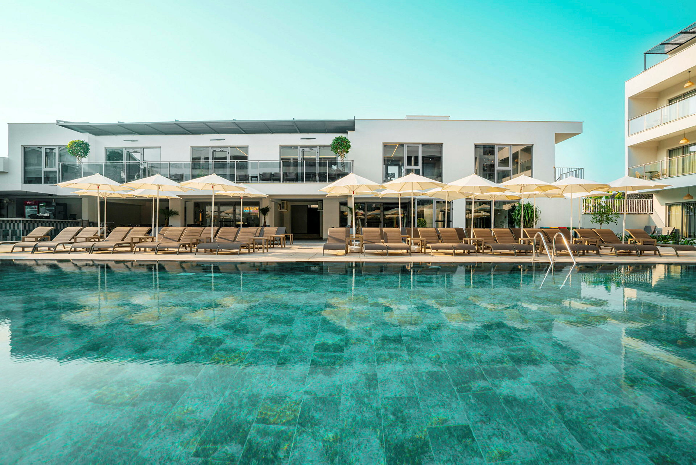 Pool med solstolar och parasoller framför en modern byggnad. (AI-genererad text)