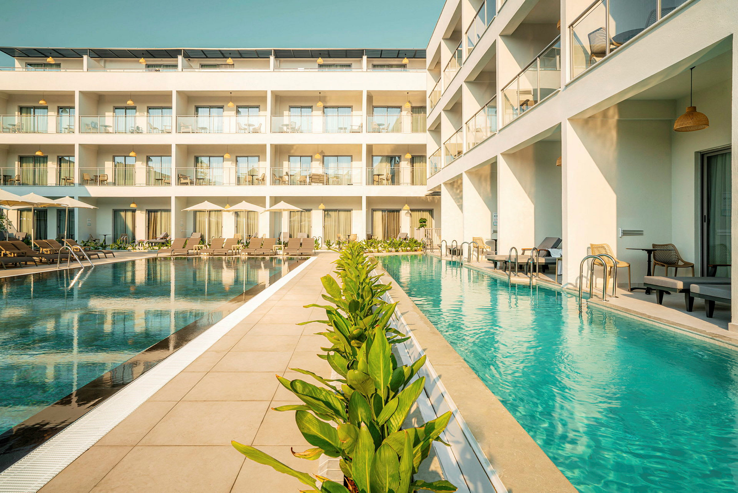 Bild av hotell med pool framför byggnaden med solstolar och gröna växter. (AI-genererad text)