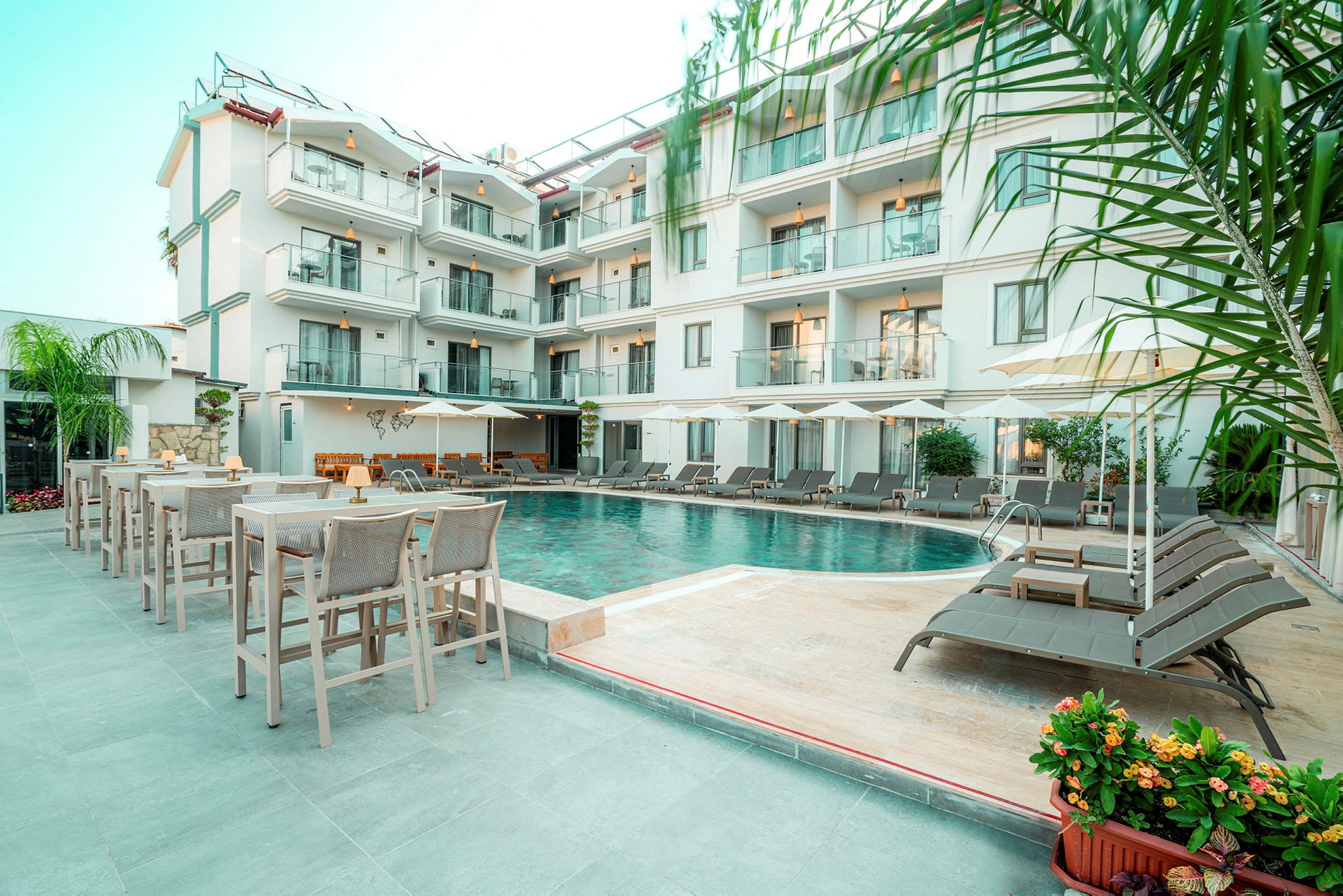 Bild på hotell med flera våningar och en pool omgiven av solstolar och bord. (AI-genererad text)