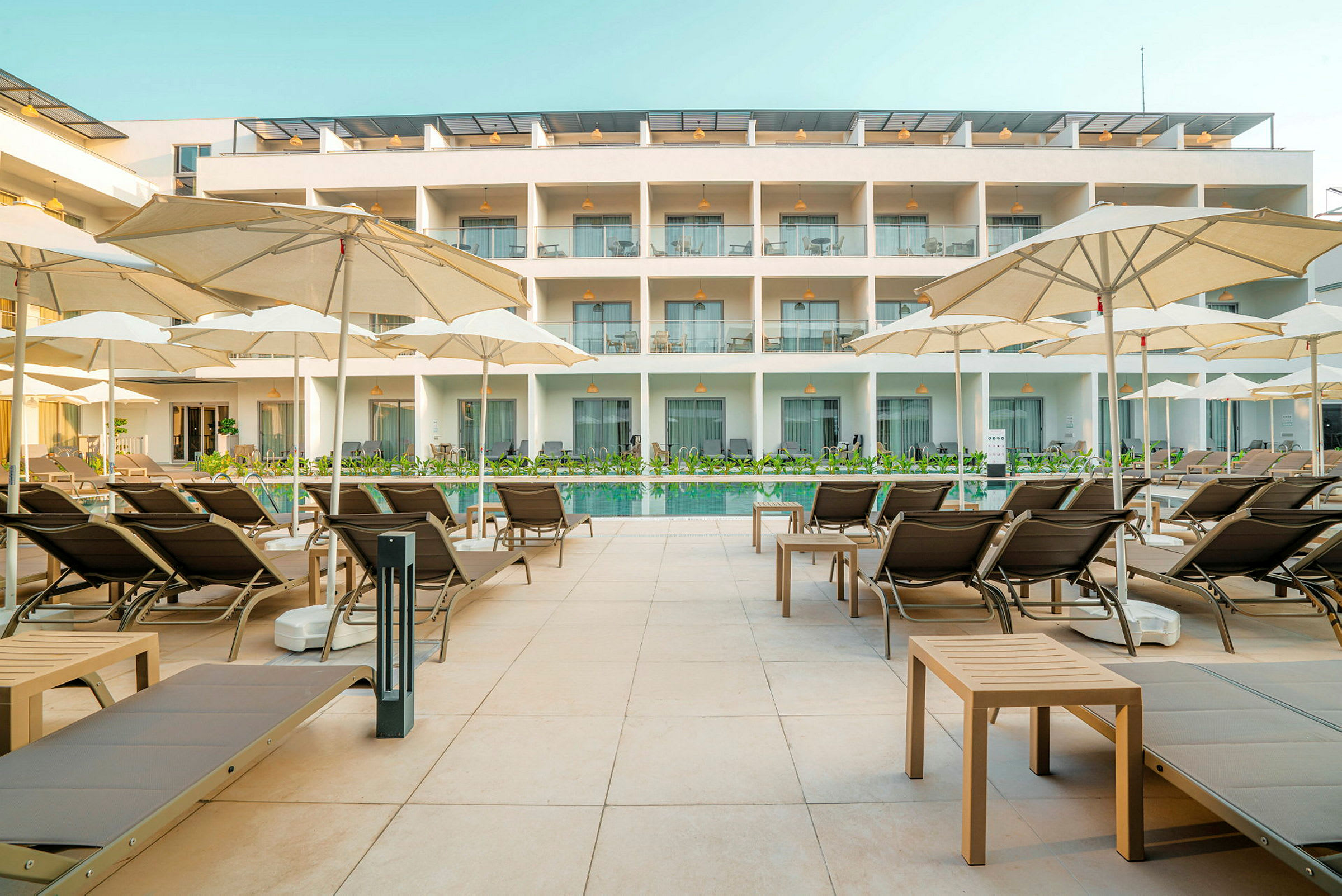 Solstolar och parasoller vid en pool framför en hotellbyggnad. (AI-genererad text)
