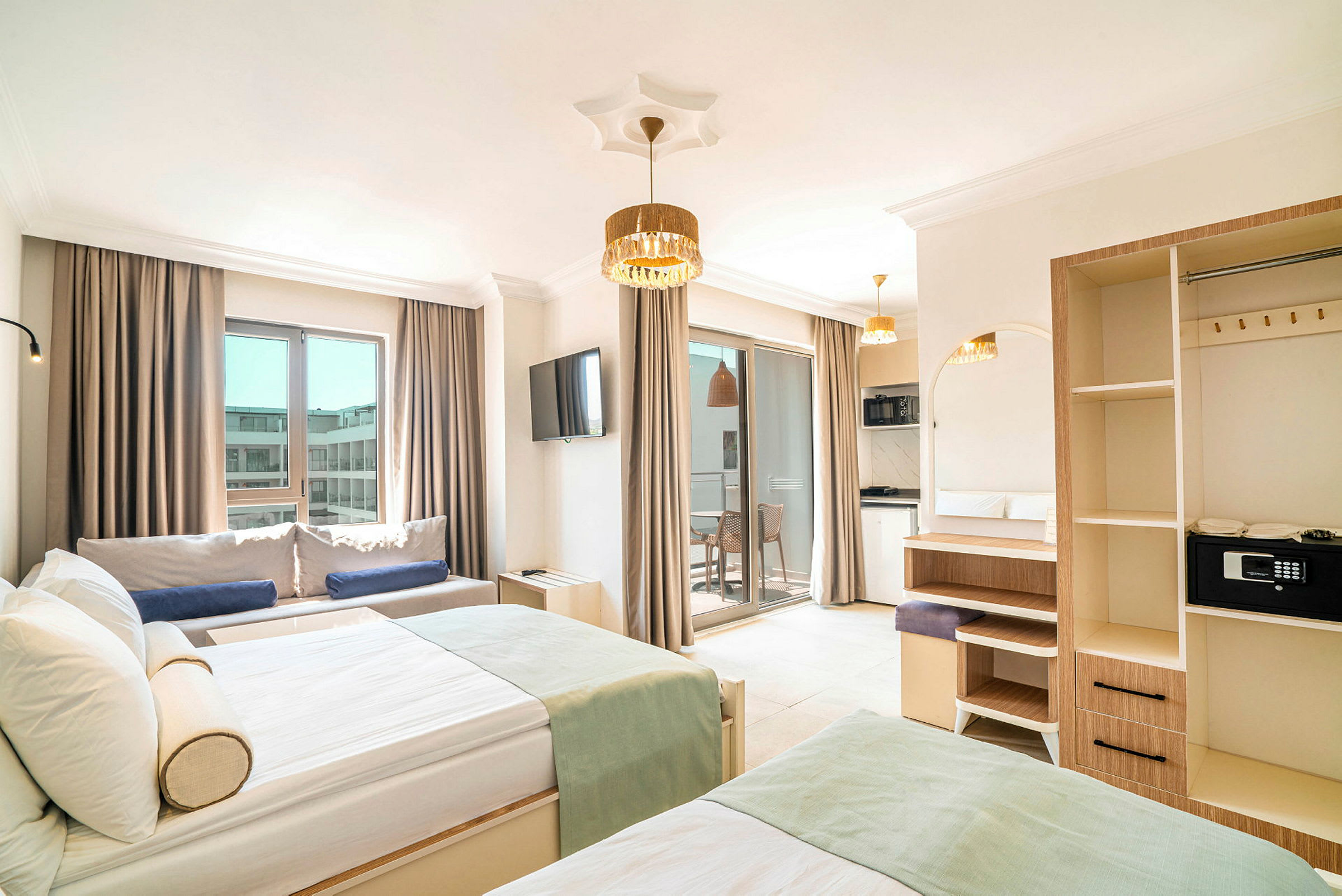 Bild på ett hotellrum med moderna möbler, två sängar, en soffa, ett TV och en balkong med ljusa gardiner. (AI-genererad text)