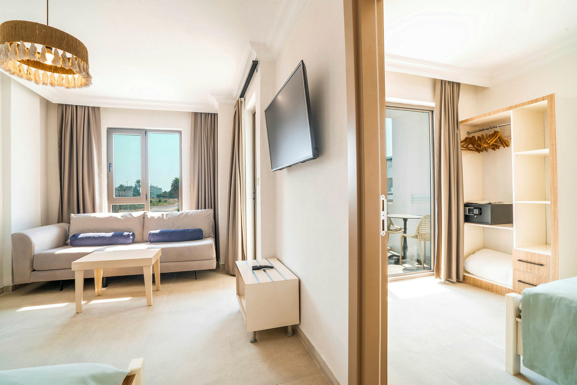 Bild på ett ljust hotellrum med soffa, bord, TV och öppen garderob. (AI-genererad text)