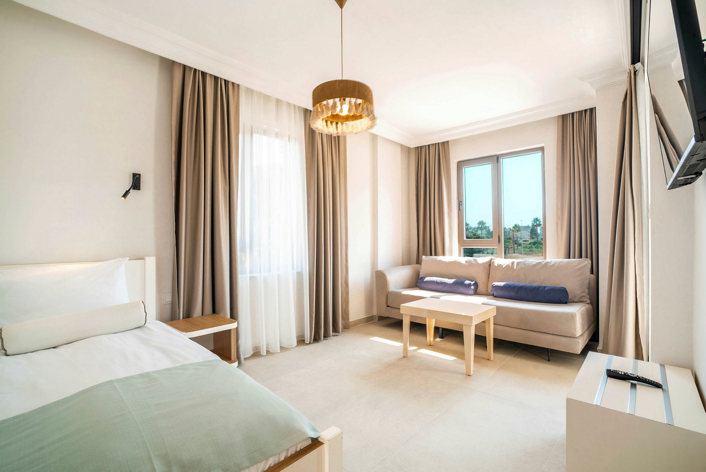 Ett hotellrum med en säng, en soffa, ett bord och stora fönster. (AI-genererad text)
