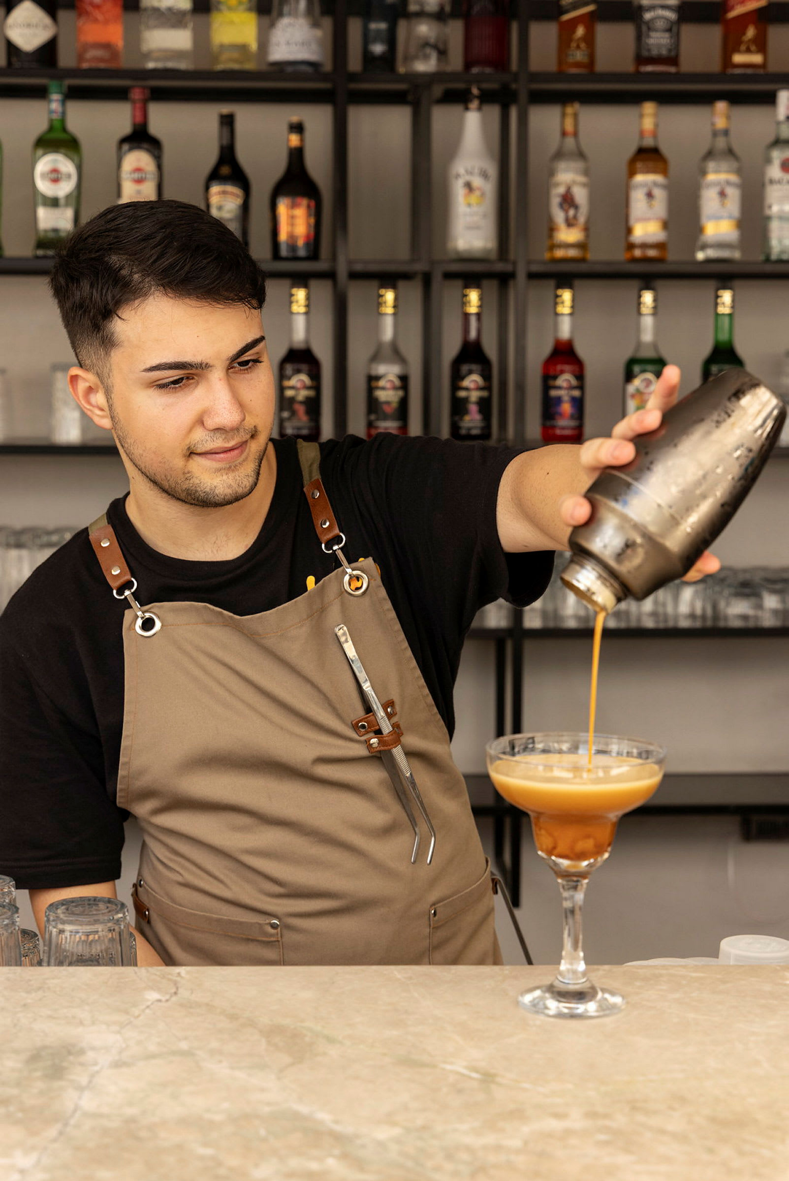 En bartender häller en drink från en shaker i ett cocktailglas. (AI-genererad text)
