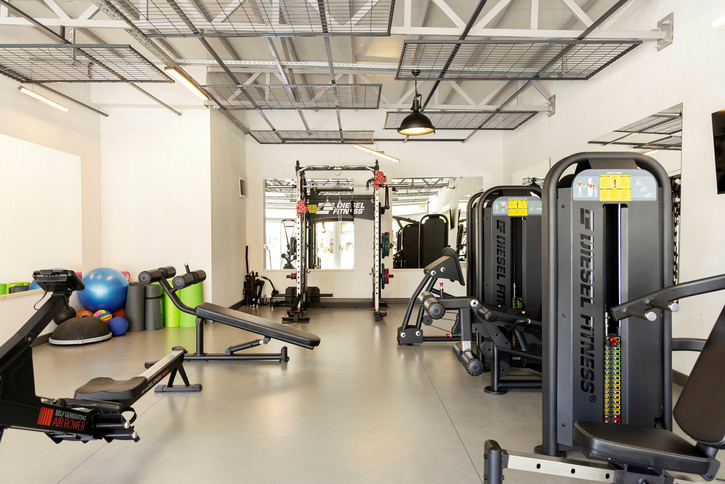 Ett gym med olika träningsmaskiner, träningsbänkar och tillbehör som medicinbollar och fitnessbollar. (AI-genererad text)