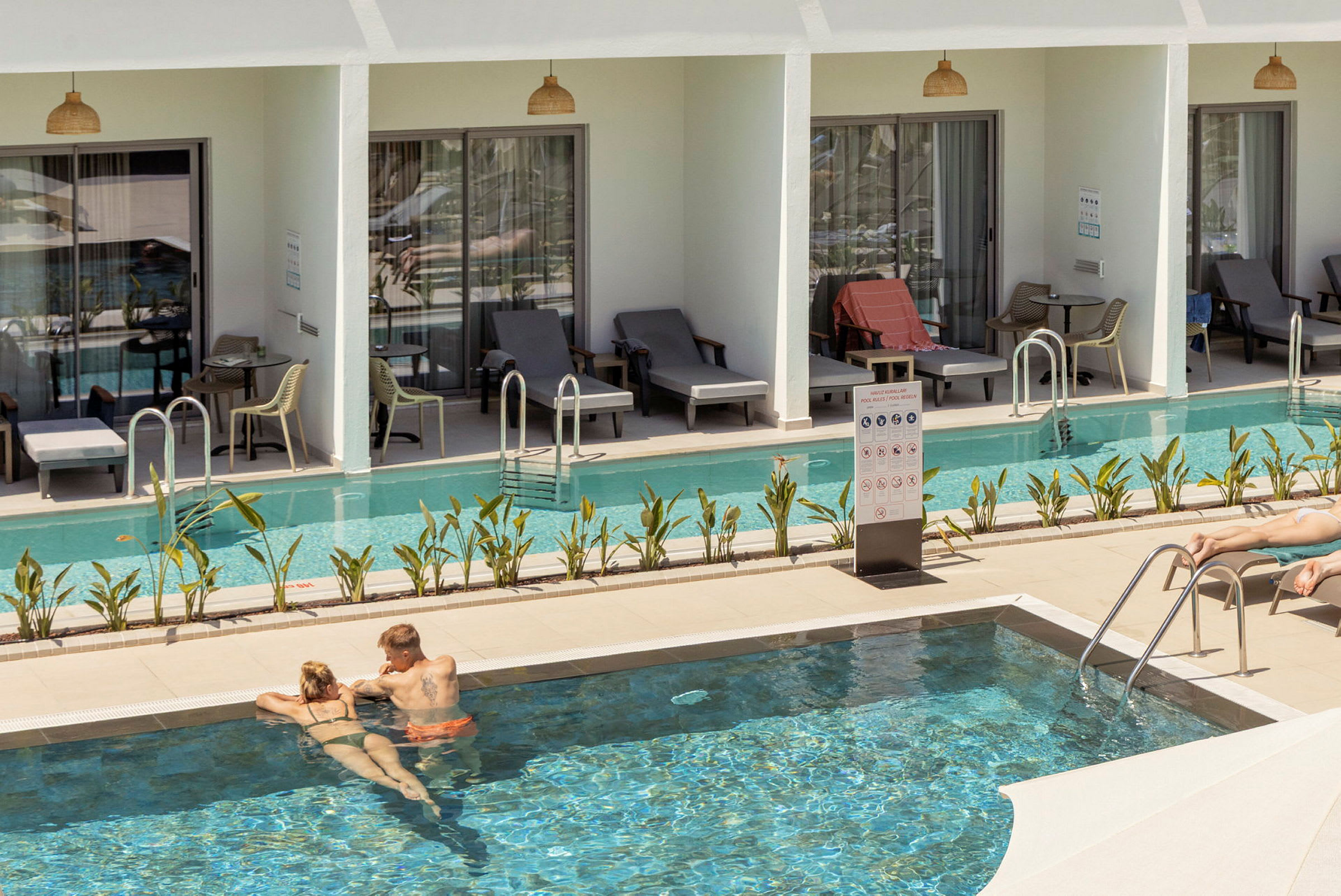 Bild som visar en pool omgiven av solstolar och rum med direkt poolaccess. (AI-genererad text)