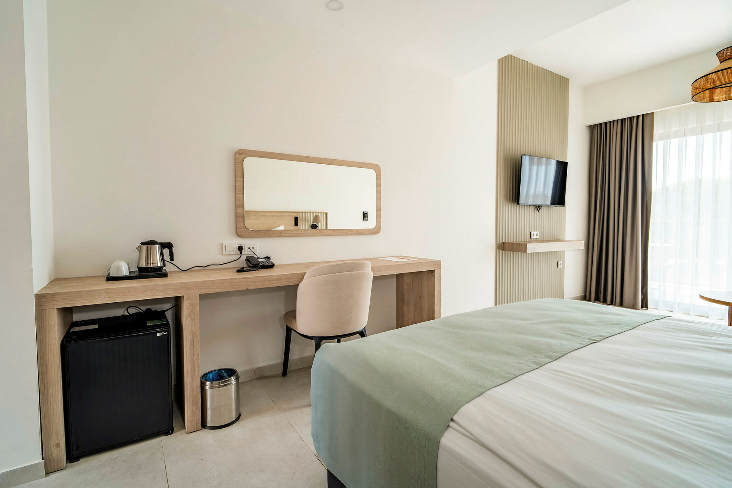 Ett hotellrum med skrivbord, spegel, stol, säng, minikylskåp och TV. (AI-genererad text)