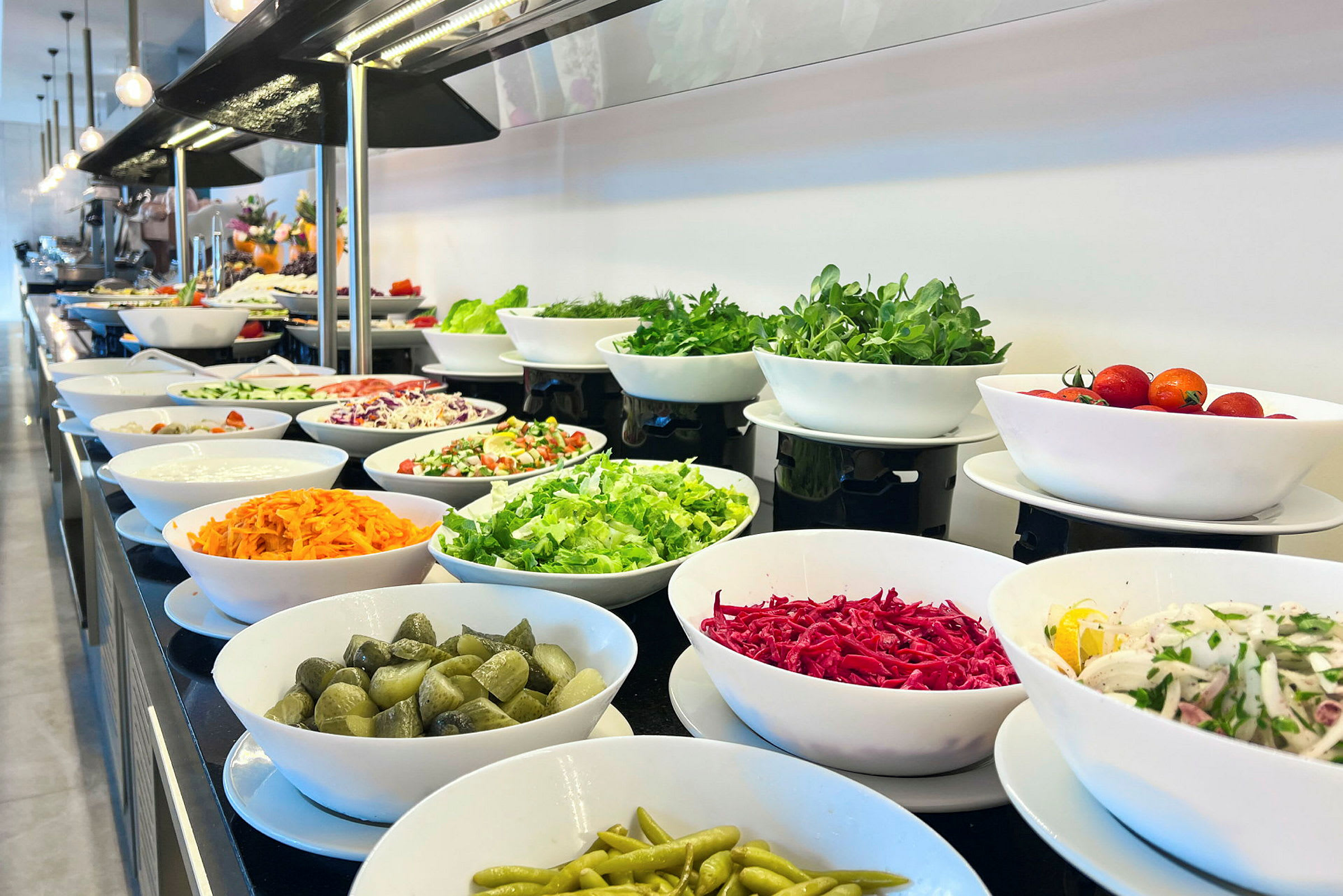 En buffé av sallad och grönsaker i vita skålar. (AI-genererad text)