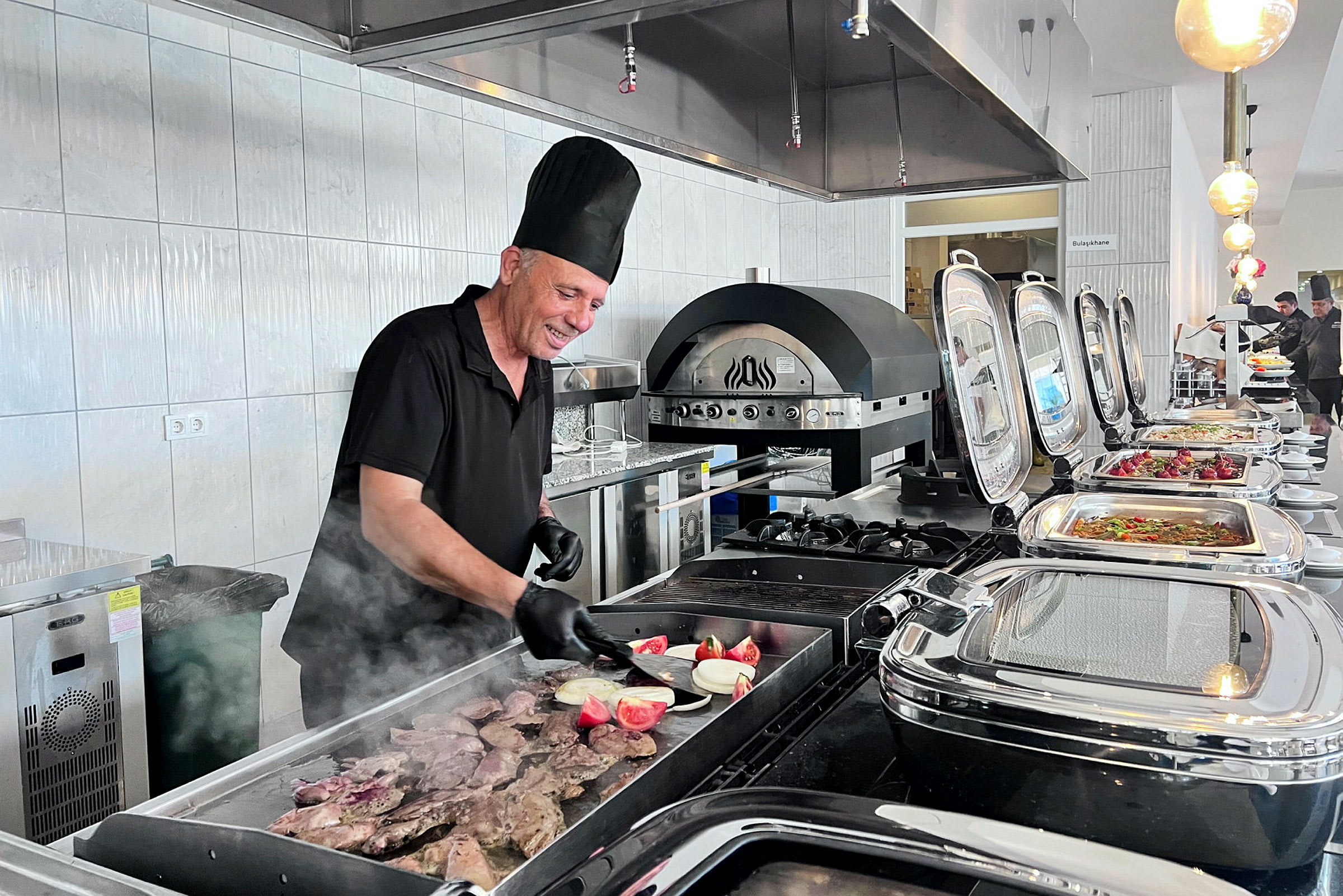 En kock lagar mat på en grill i en buffémiljö. (AI-genererad text)