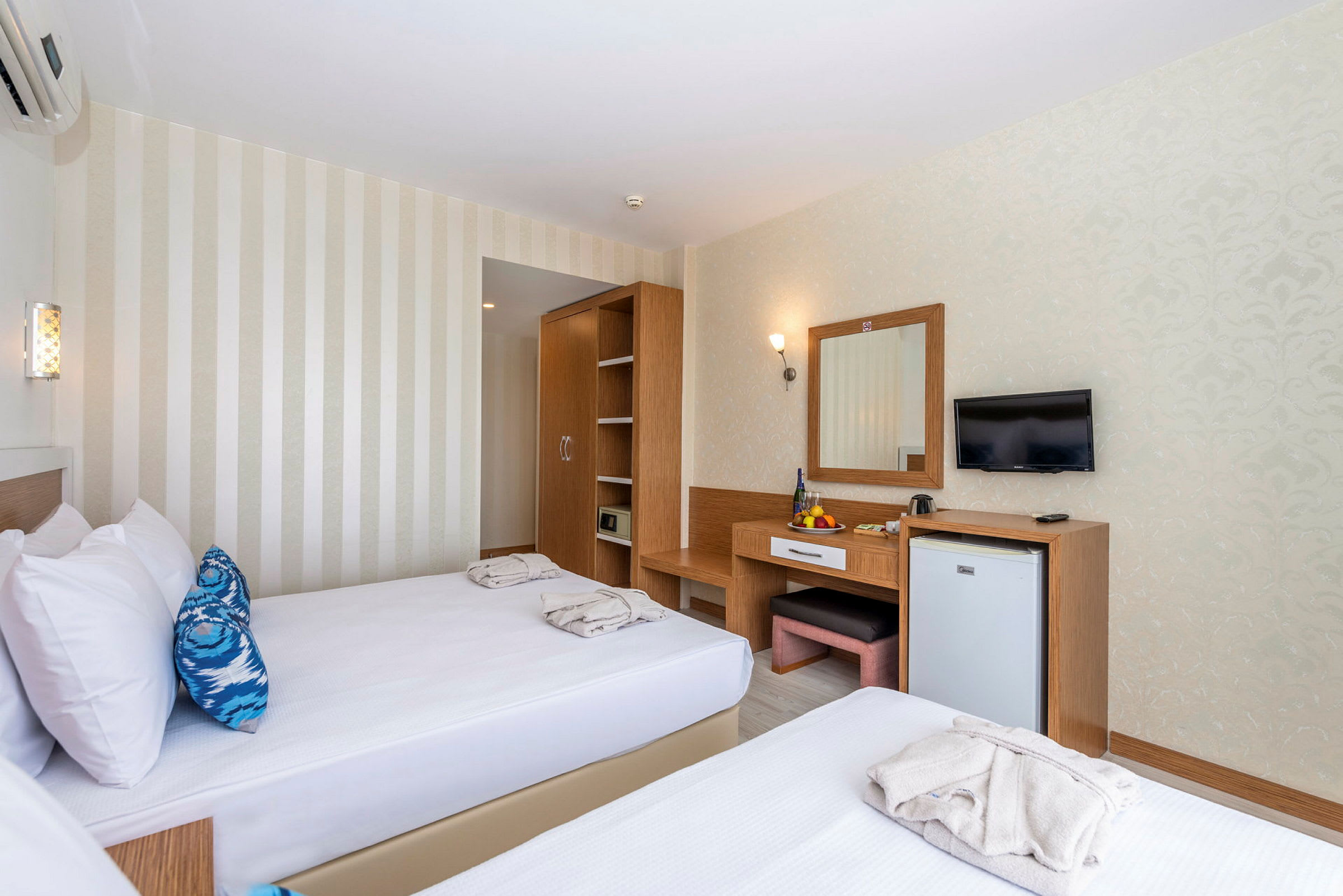 Hotellrum med två enkelsängar, en garderob, ett skrivbord med spegel och en väggmonterad TV. (AI-genererad text)