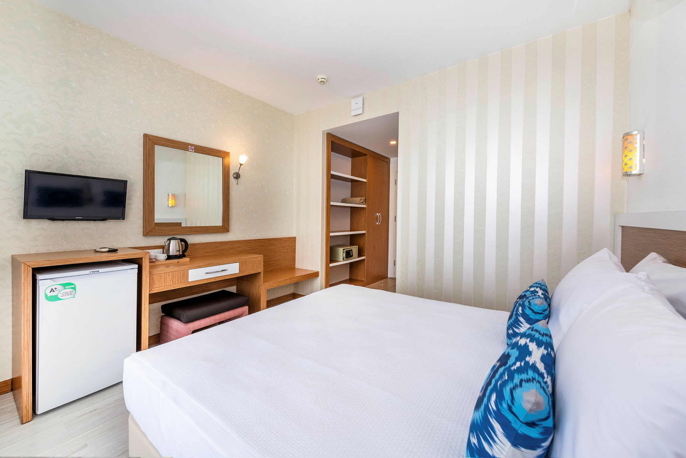 Inredning av ett hotellrum med en dubbelsäng, skrivbord, kylskåp och en TV monterad på väggen. (AI-genererad text)