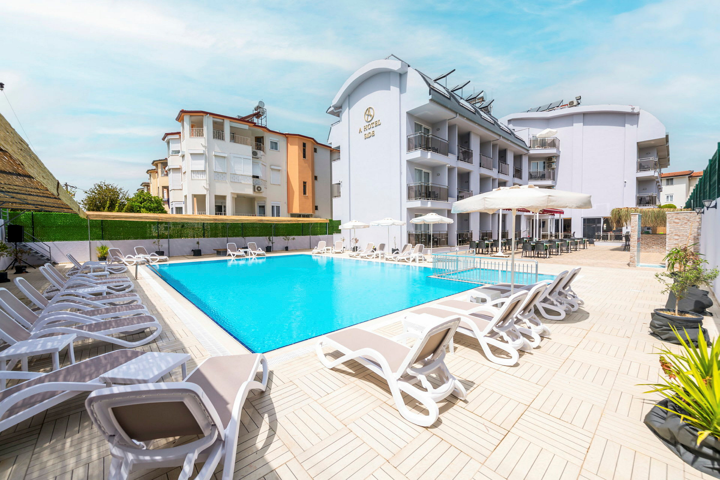 Hotellets poolområde med solstolar, parasoller och byggnaden i bakgrunden. (AI-genererad text)