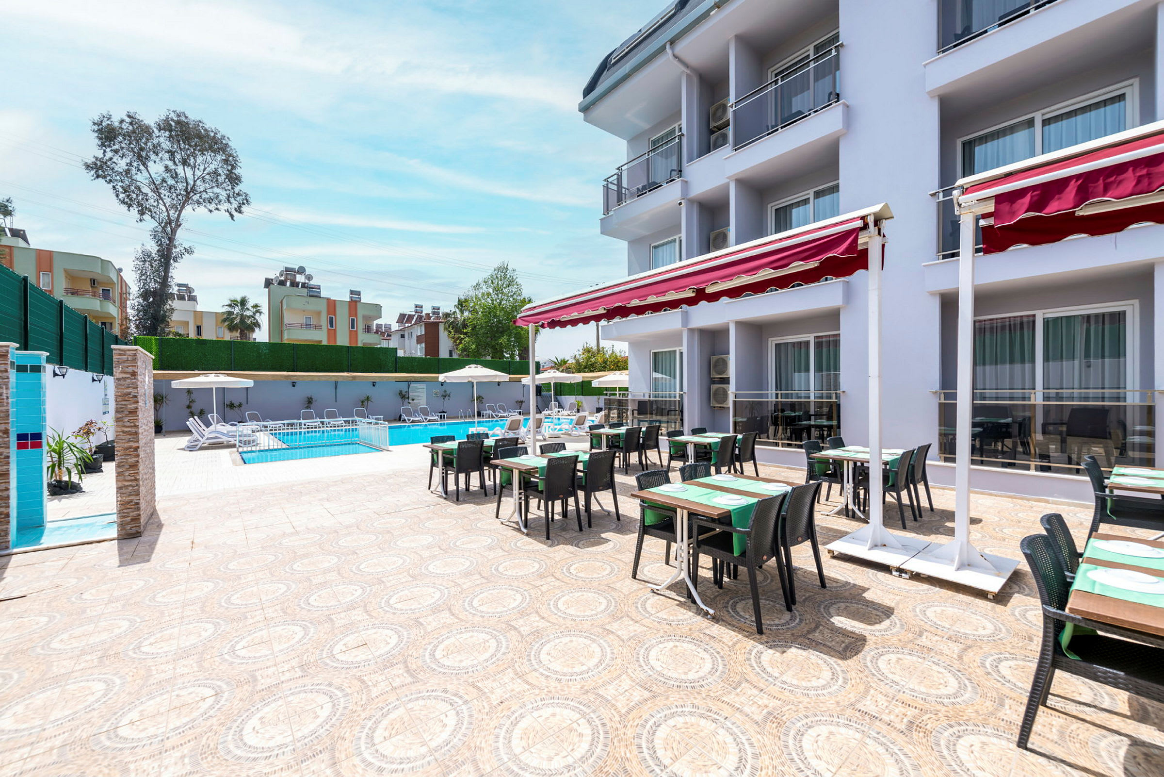 Uteplats med bord och stolar framför ett hotell, poolområde i bakgrunden. (AI-genererad text)