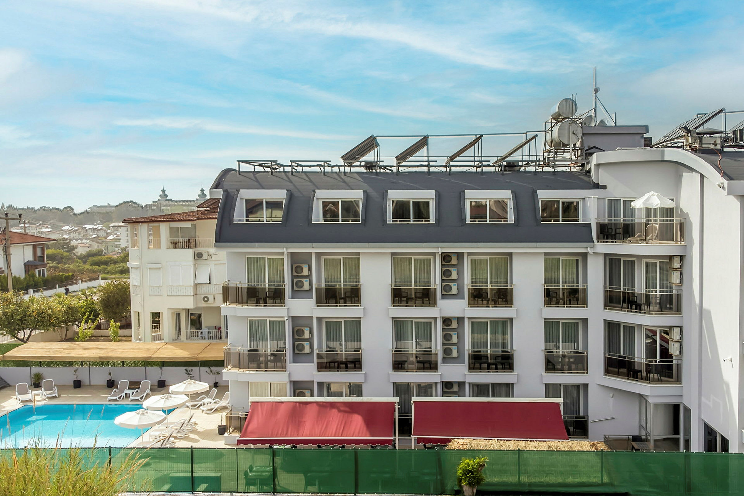 Ett hotell med vit fasad och flera fönster och balkonger, en pool framför byggnaden. (AI-genererad text)