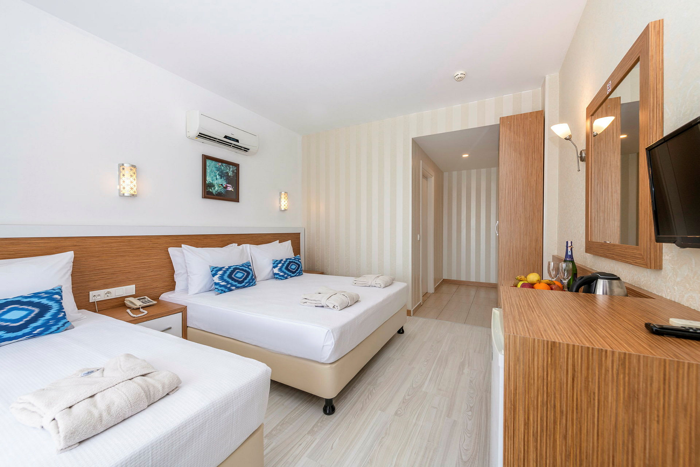 Ett ljust och modernt hotellrum med två sängar, en spegel samt ett skrivbord med frukt och dryck. (AI-genererad text)