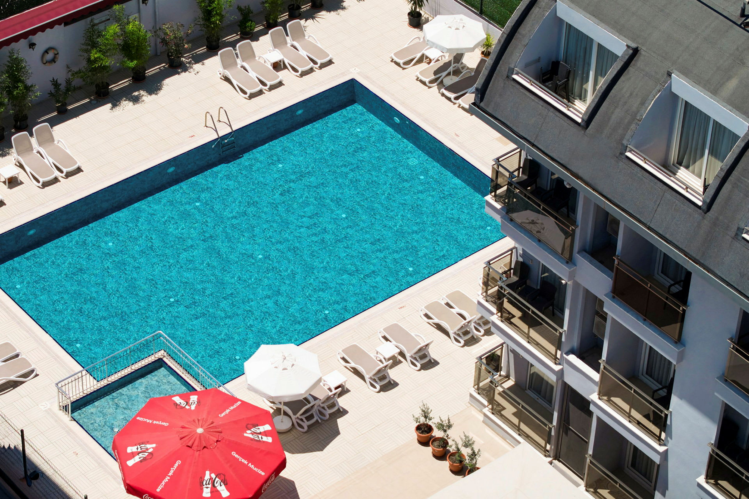En hotellpool med solsängar och parasoller vid ett flerbostadshus. (AI-genererad text)