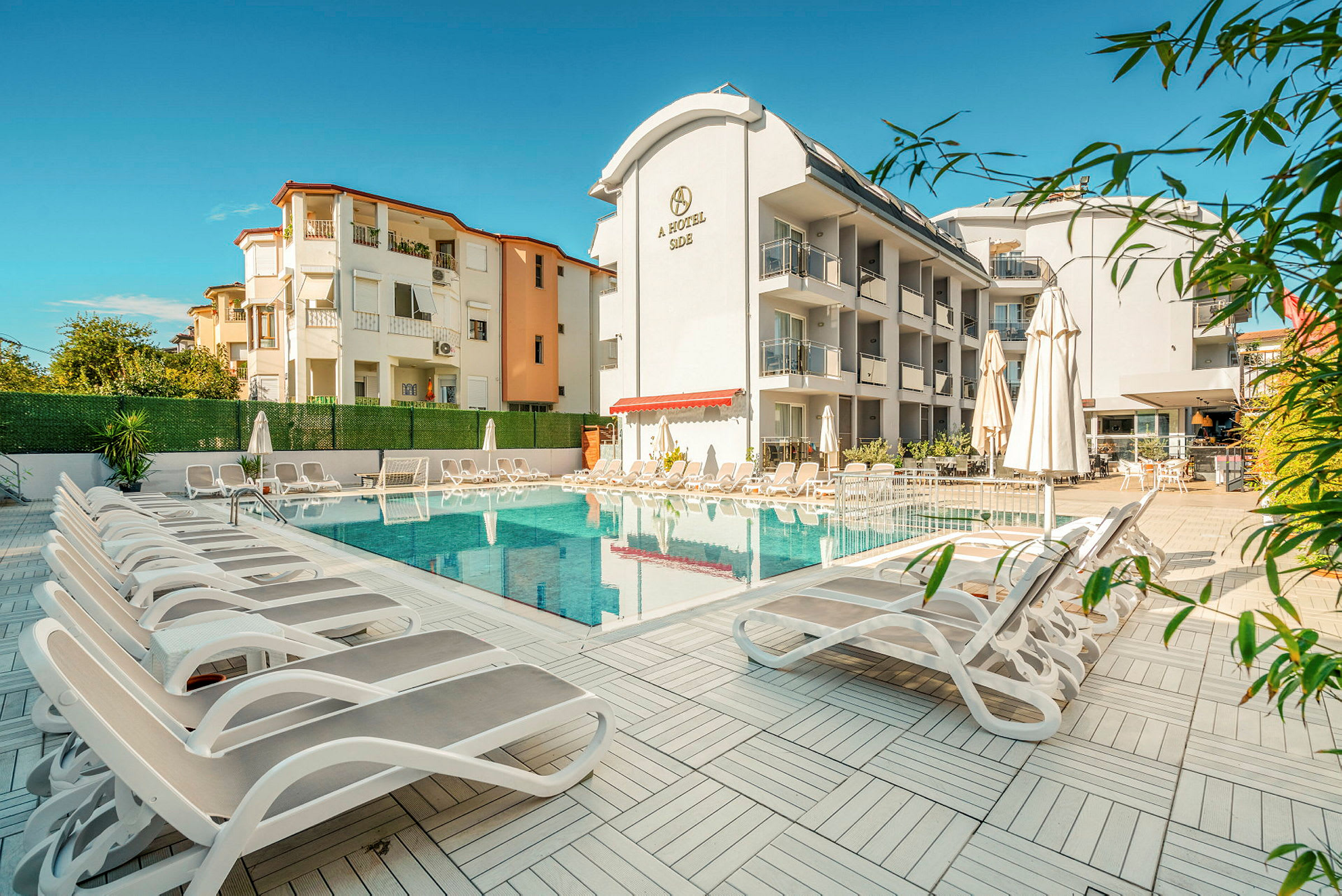 Bild av hotellpoolområde med solstolar och parasoller framför byggnader. (AI-genererad text)