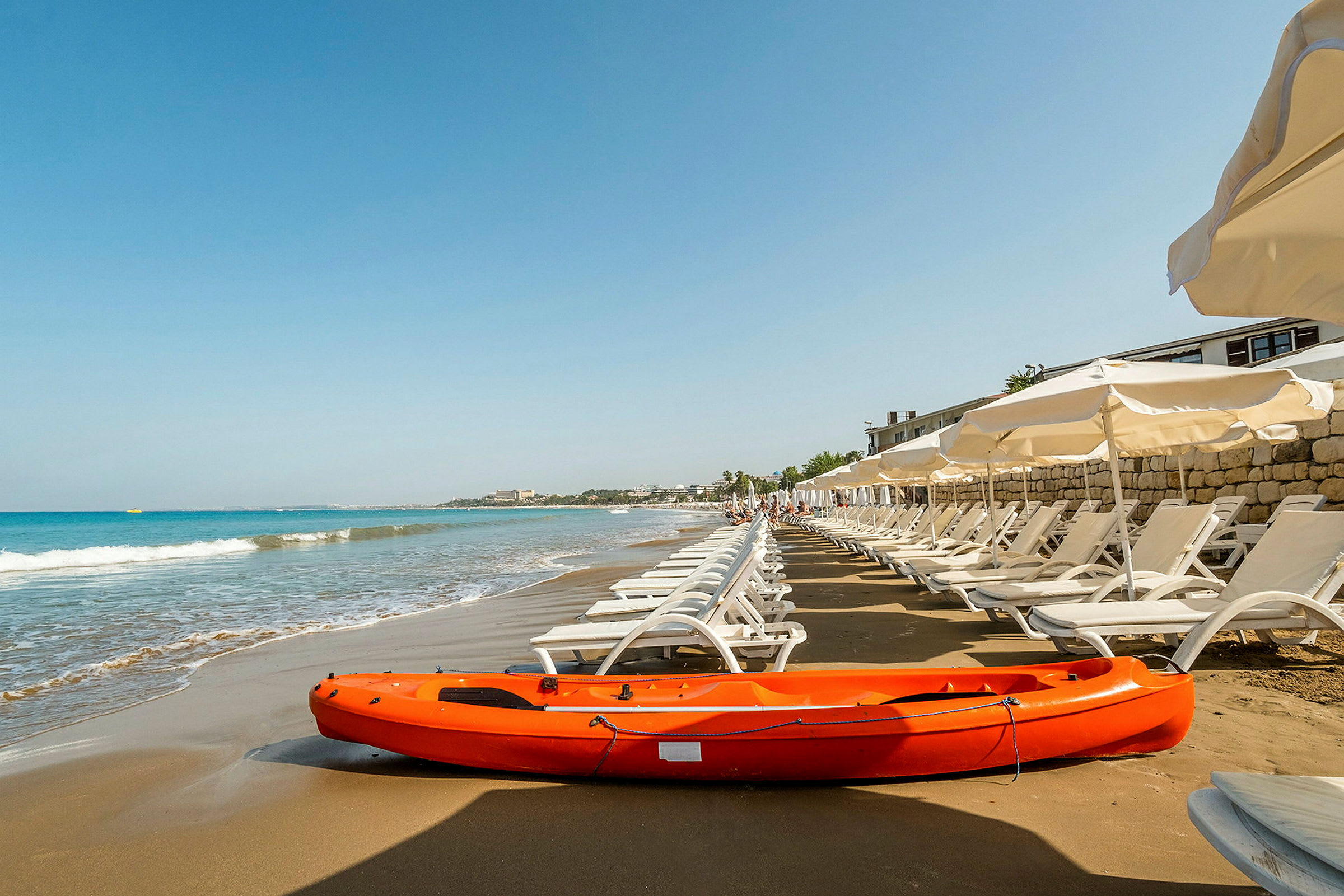 Strand med solstolar och parasoller, en orange kajak i förgrunden. (AI-genererad text)