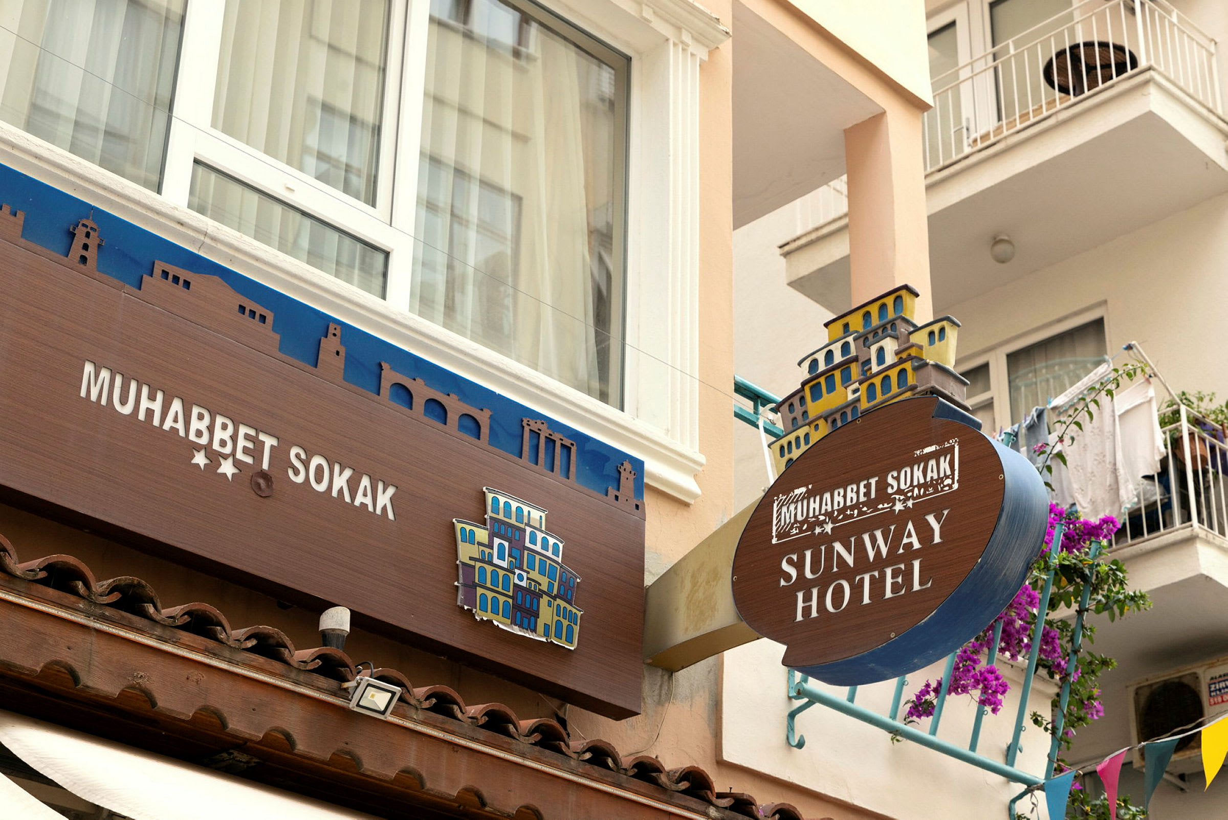 Bild på fasaden till ett hotell med skyltar som visar namnen 'Muhabbet Sokak' och 'Sunway Hotel'. (AI-genererad text)