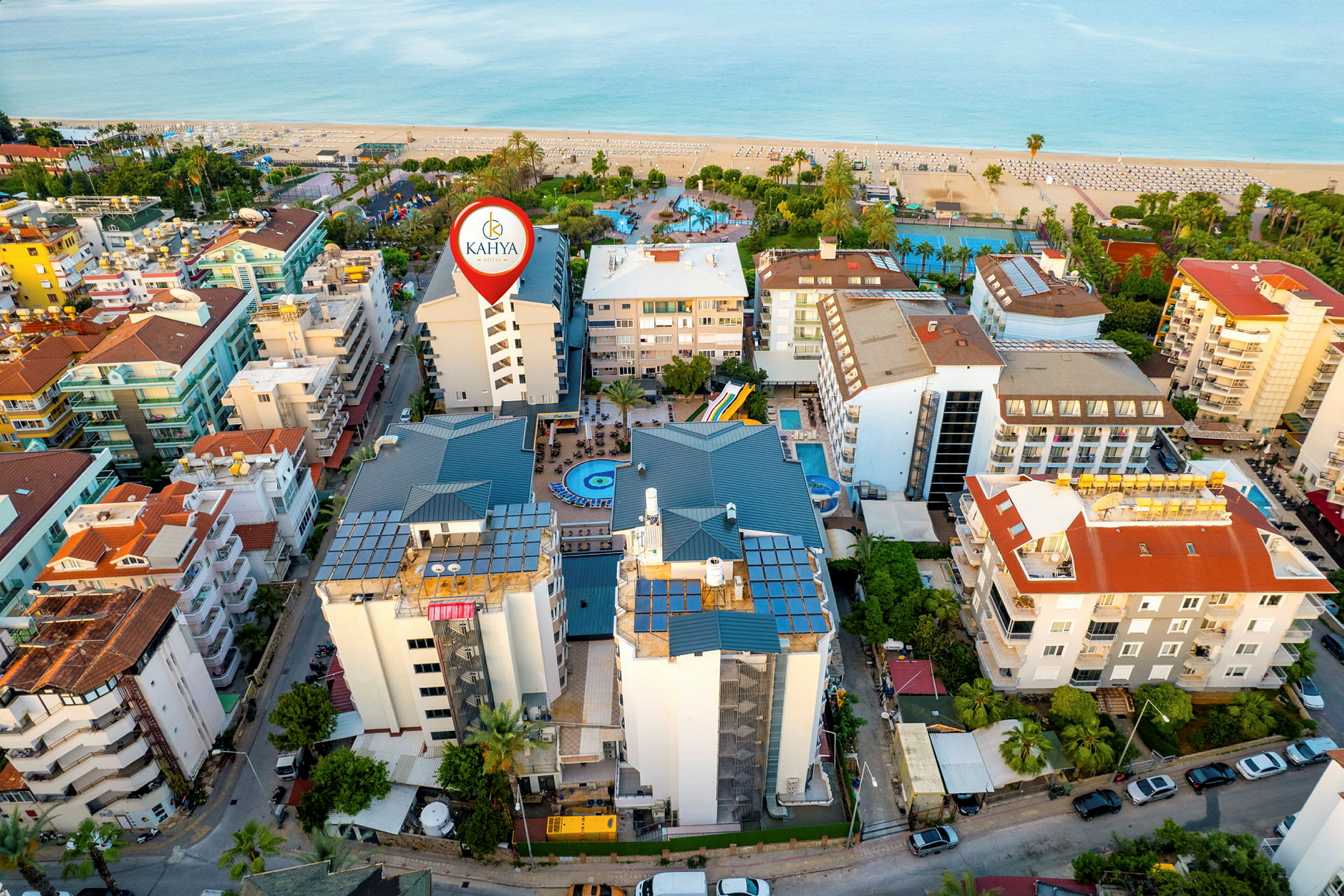 Flygbild av ett stadsområde vid stranden med flera byggnader, en pool och byggnaden markerad som Kahya Hotel. (AI-genererad text)