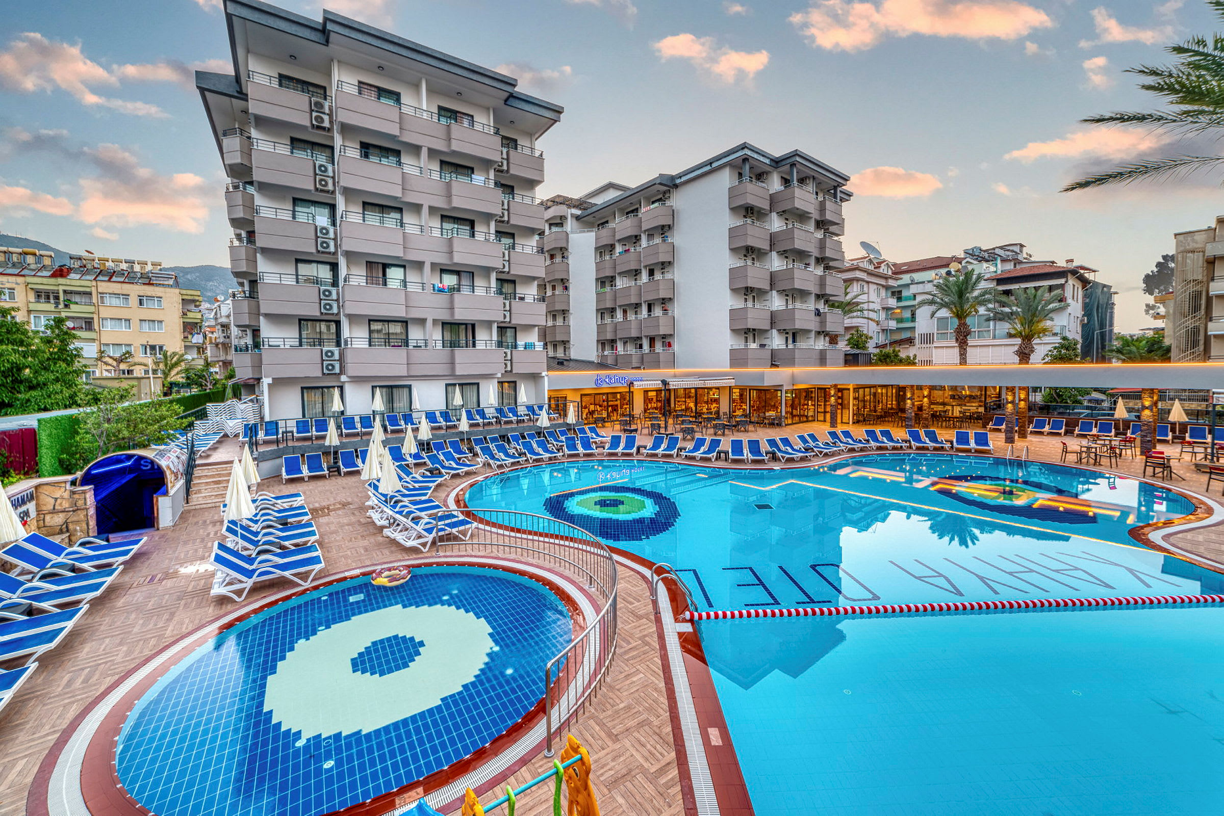 Hotellområde med pooler, solstolar och byggnader i bakgrunden. (AI-genererad text)