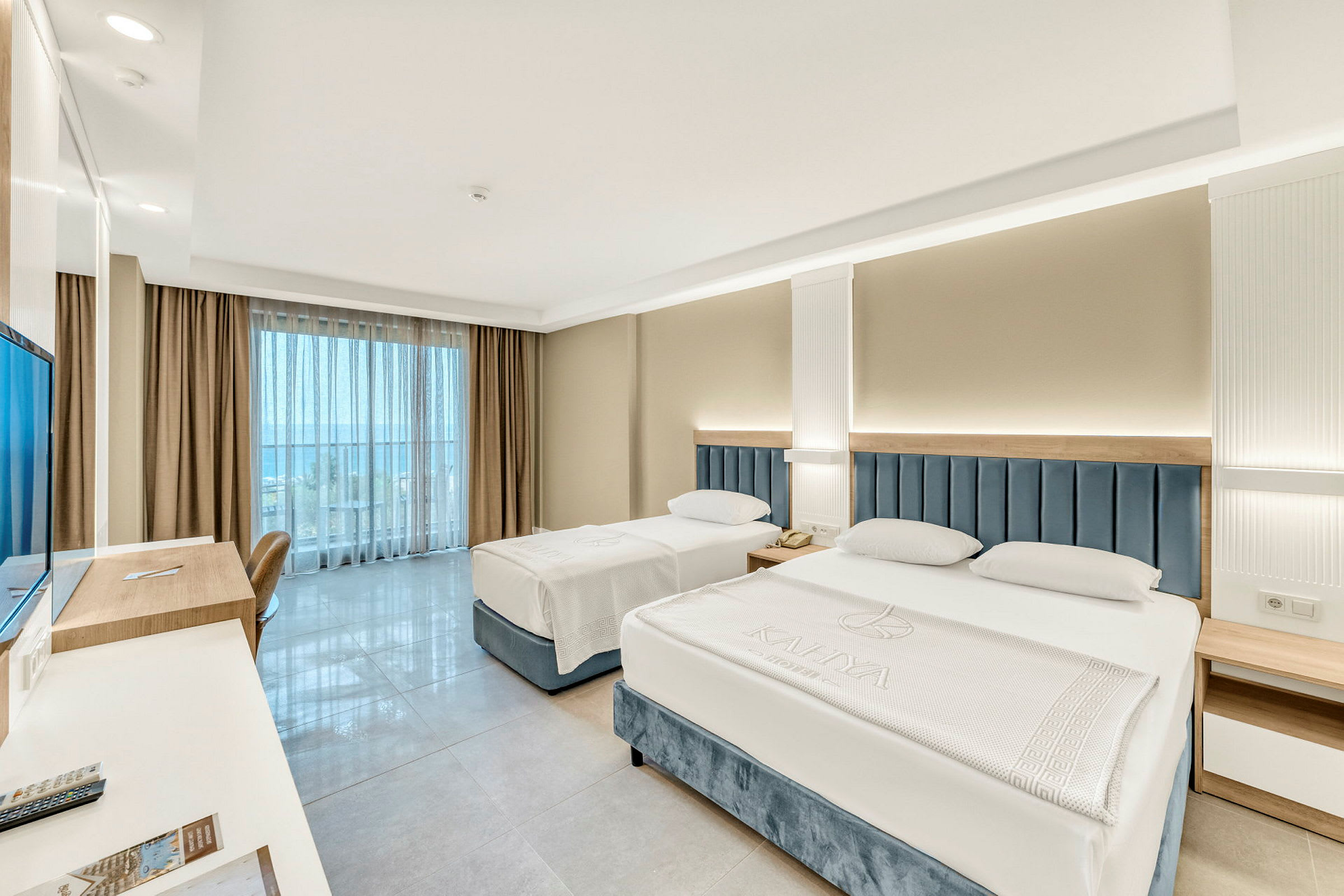 Hotellrum med två sängar, skrivbord och utsikt mot balkong. (AI-genererad text)