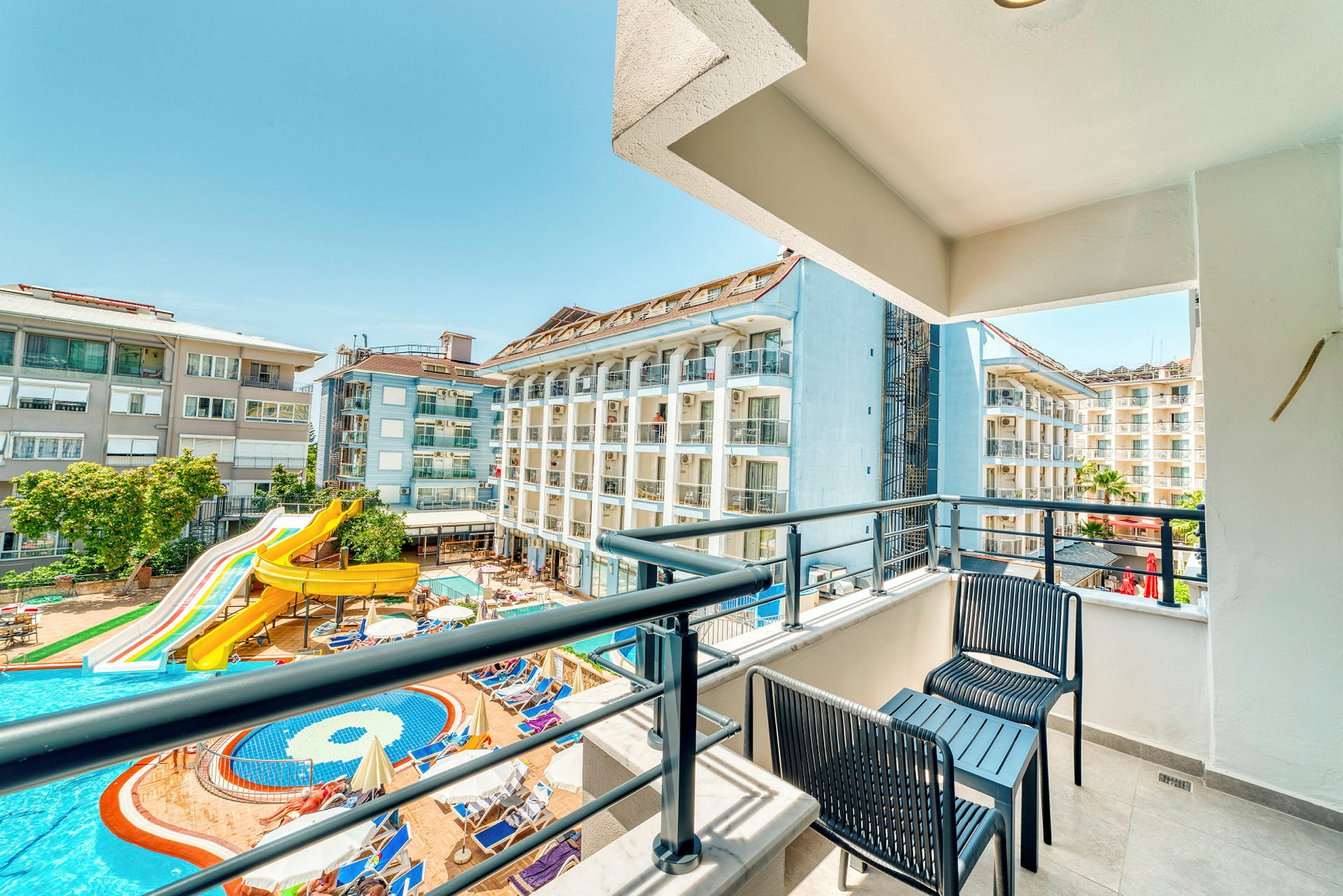 Balkong med utsikt över hotellbyggnader och en pool med vattenrutschbana. (AI-genererad text)