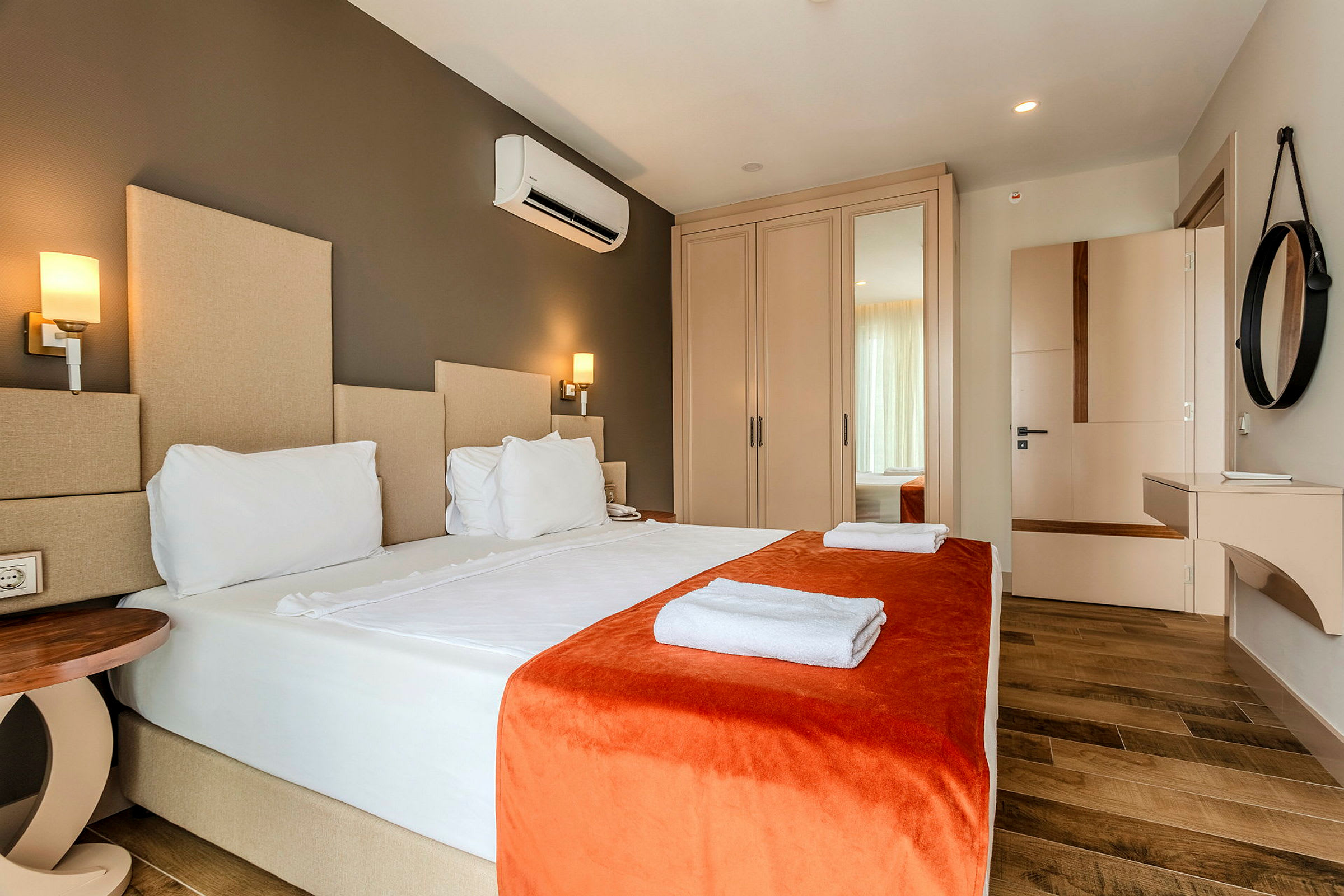 En hotellrum med en dubbelsäng klädd i vita lakan och orange överkast, med handdukar placerade på sängen. (AI-genererad text)
