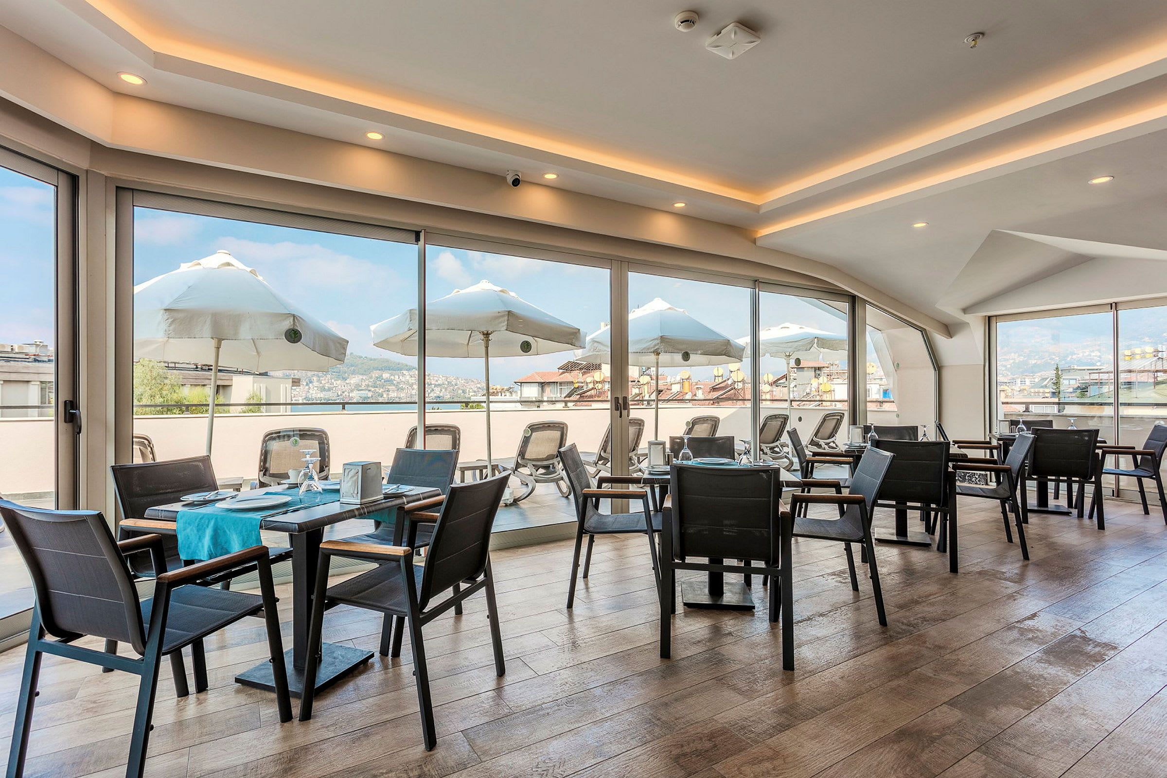 En restaurang med glasväggar och utsikt över solparasoller och omgivningar. (AI-genererad text)