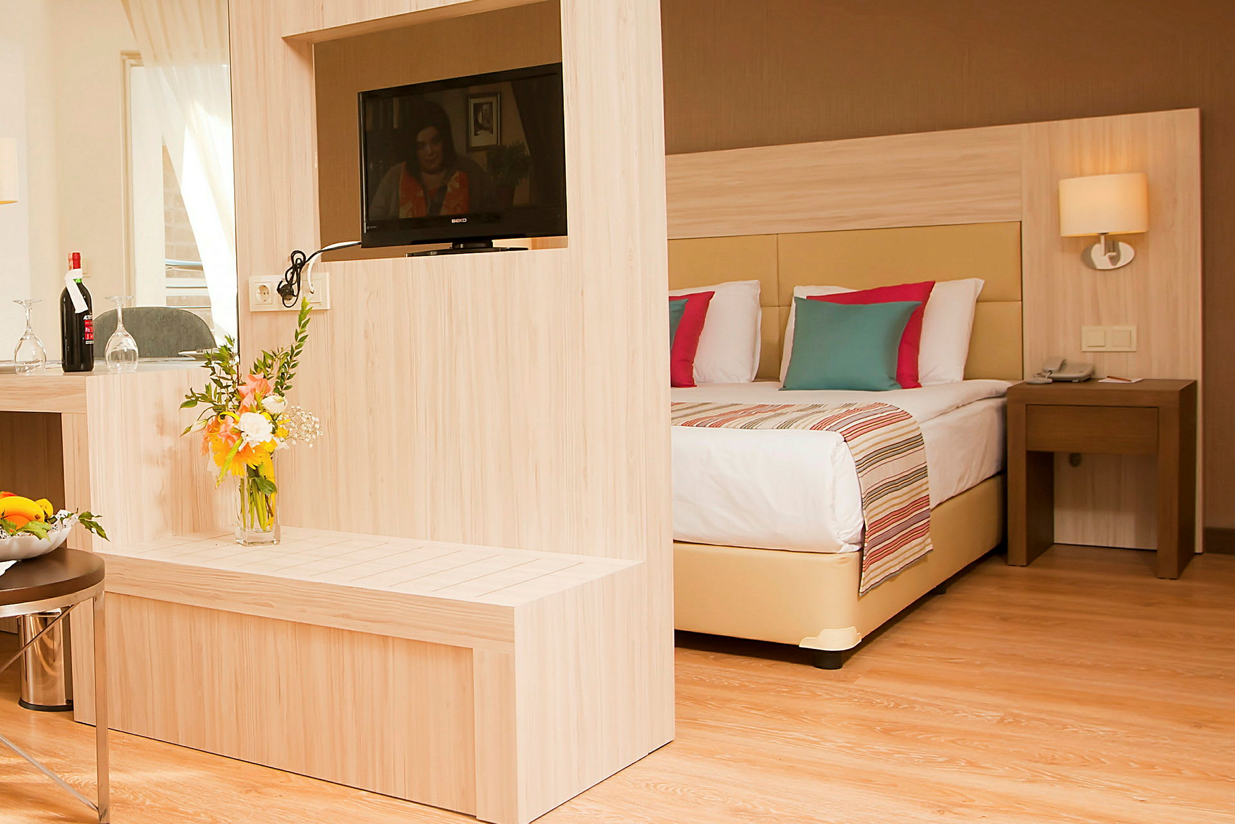 Ett hotellrum med en modern inredning, inklusive en dubbelsäng, en TV på en träpanel och en blombukett. (AI-genererad text)